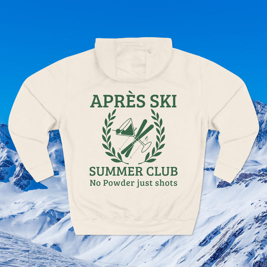 Apres Ski Summer Club An off-white hooded sweatshirt shown from the back, featuring a green graphic print that reads 'APRÈS SKI SUMMER CLUB No Powder just shots' with crossed skis and a laurel wreath. The sweatshirt is displayed against a scenic background of snowy mountains under a bright blue sky.