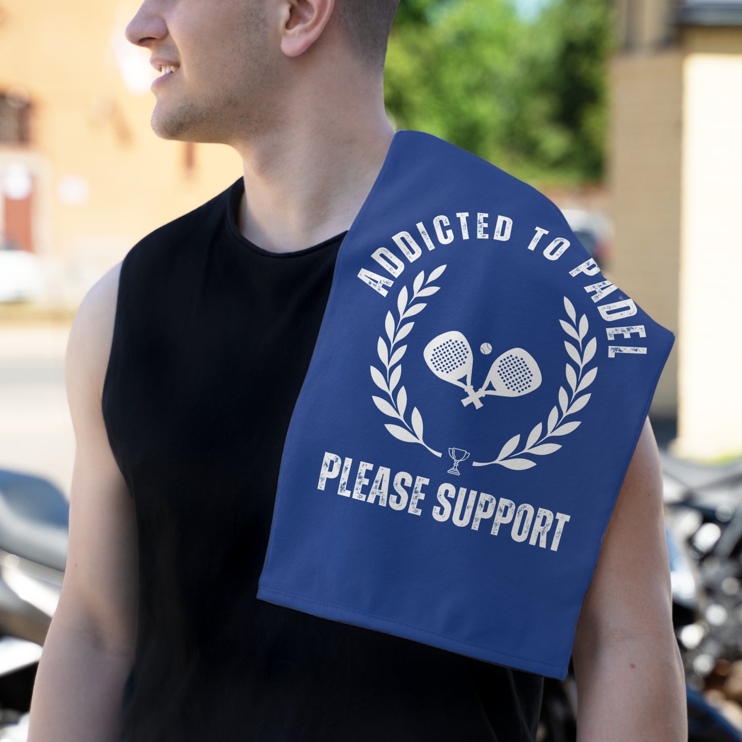 Man holding a blue towel with 'Addicted to Padel Please Support' text and tennis racket design.
