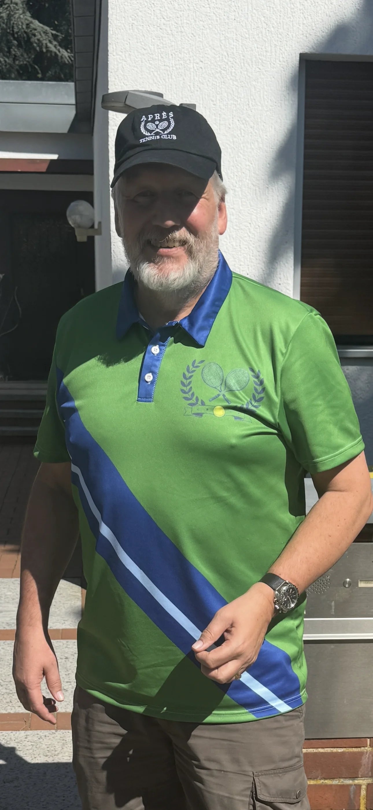 Vintage Tennis Polo Man wearing a green polo shirt with blue and white stripes, standing in front of a building.