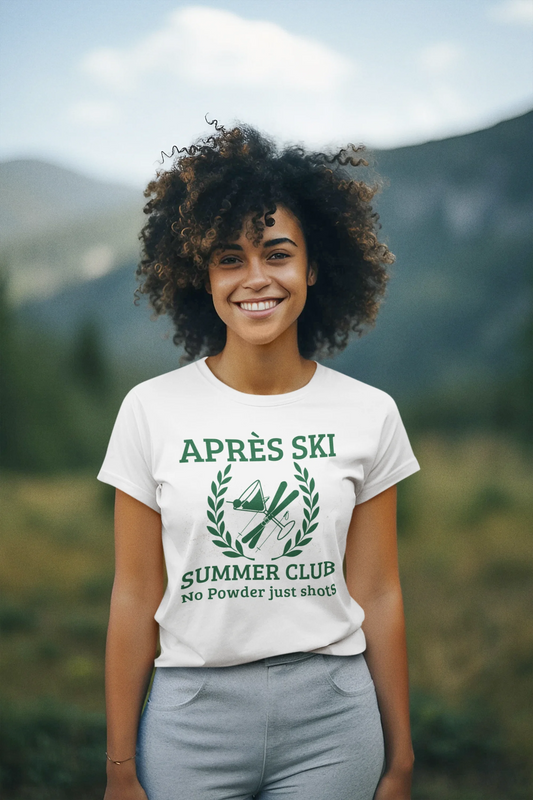Apres ski clothes ladies A smiling woman with curly hair stands outdoors in front of blurred mountains, wearing a white graphic T-shirt with green text reading 'APRÈS SKI SUMMER CLUB' and a green mountain-and-ski emblem.