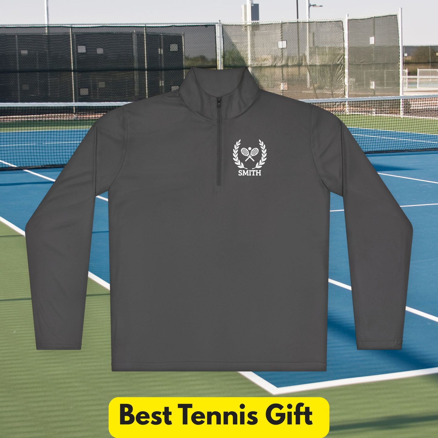 personalized tennis racket sweater A dark gray long-sleeve quarter-zip pullover with a white custom crest logo and the name 'SMITH' on the left chest, displayed against a tennis court background with a yellow 'Best Tennis Gift' banner at the bottom.