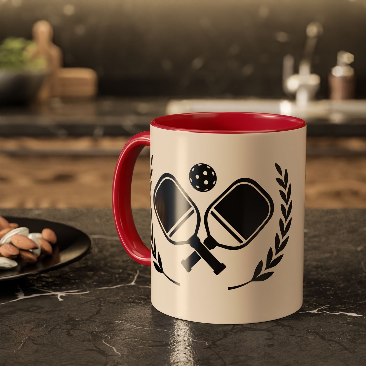 pickleball mug A ceramic mug with a red interior and handle, featuring a black graphic of crossed paddles, a ball, and laurel leaves on a cream exterior, set on a dark kitchen countertop.