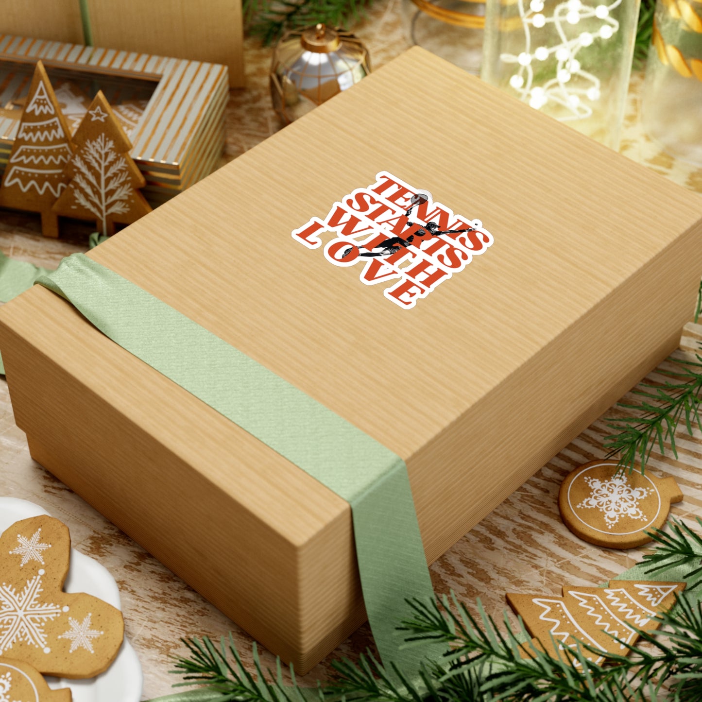 Gift box with a green ribbon and decorative label on a festive background with cookies and lights.