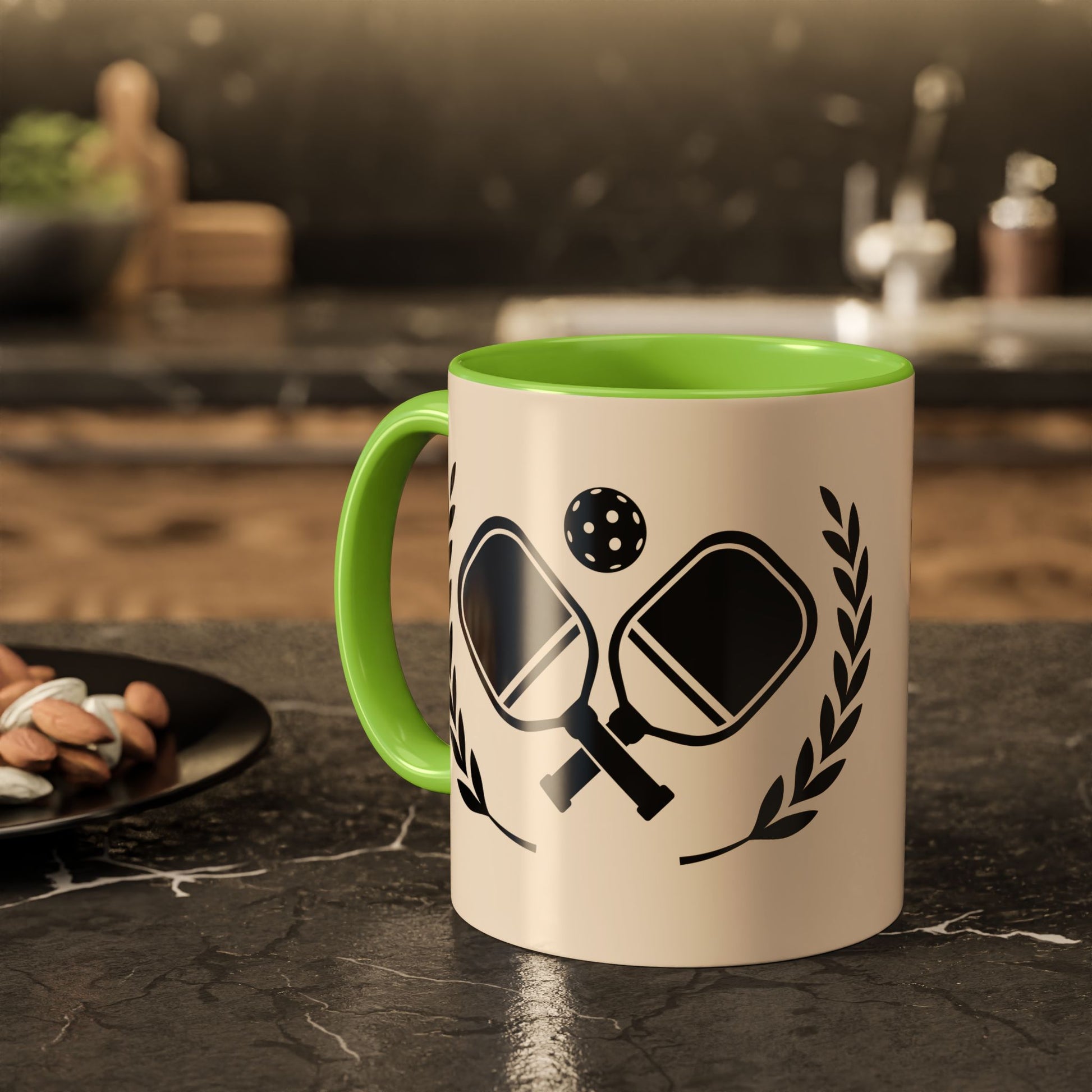 pickleball mug A ceramic mug with a cream-colored exterior and a bright green handle/interior, featuring a black ping-pong graphic with paddles, a ball, and laurel leaves. The mug is set on a dark marble countertop with a blurred kitchen background.