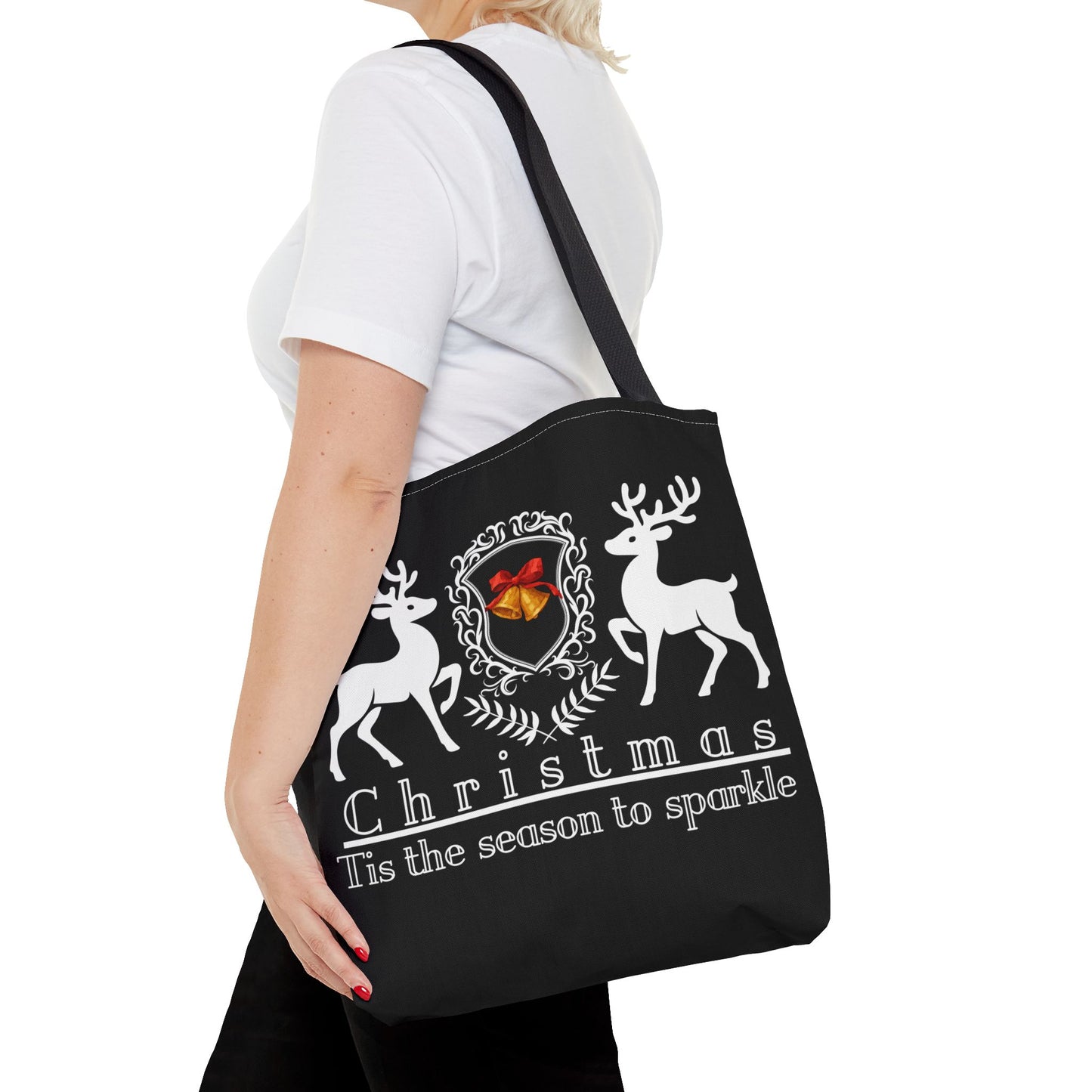 Black tote bag with reindeer design and text held by a person on a white background