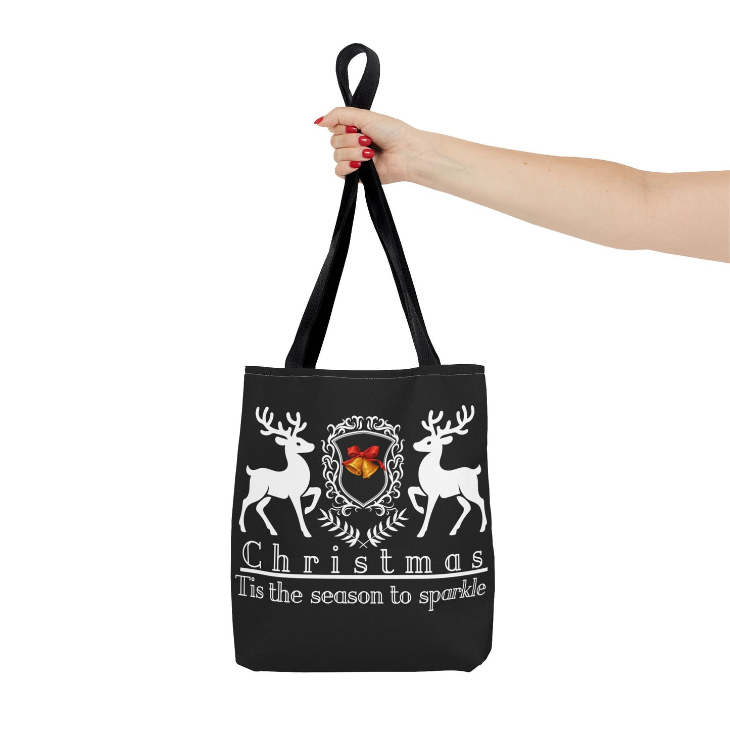 Black tote bag with Christmas design featuring deer and text, held by a hand on a white background.