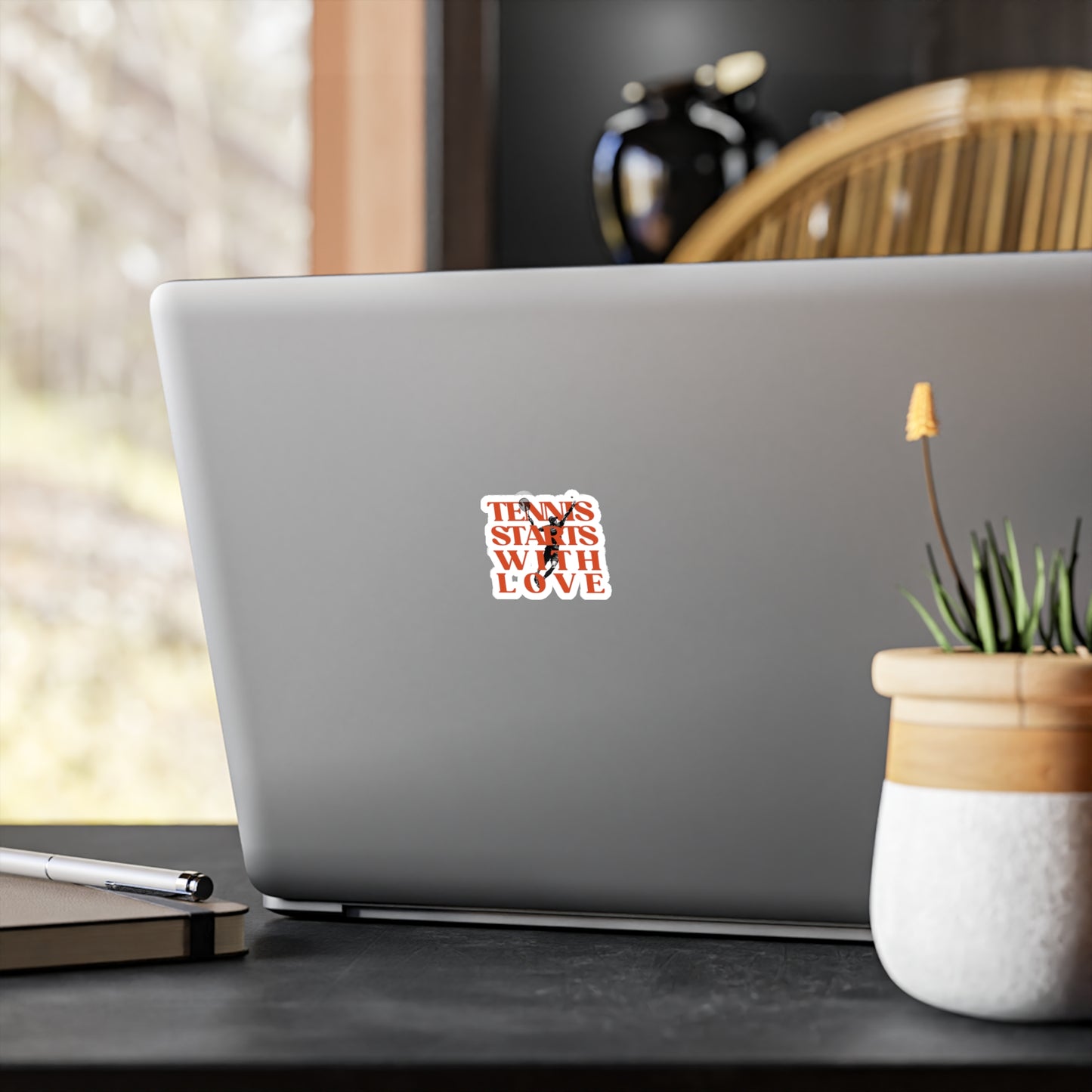 Laptop with a sticker on a desk with a plant and pen