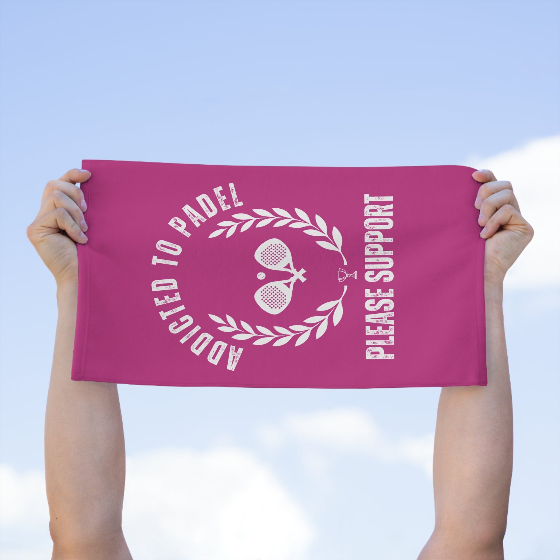 Pink towel with white text and graphics held up against a blue sky