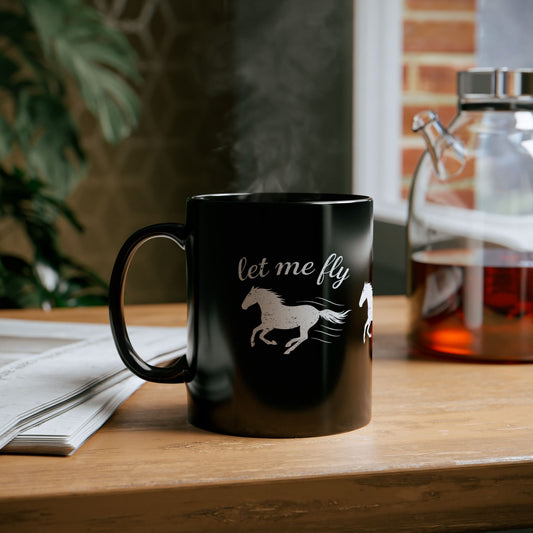 Black mug with horse design and 'let me fly' text on a wooden table.