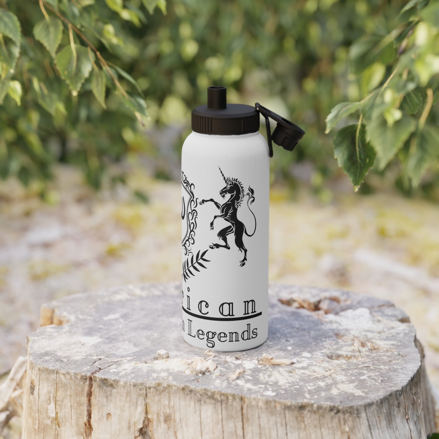 White water bottle with black unicorn design and text on a wooden stump with greenery in the background