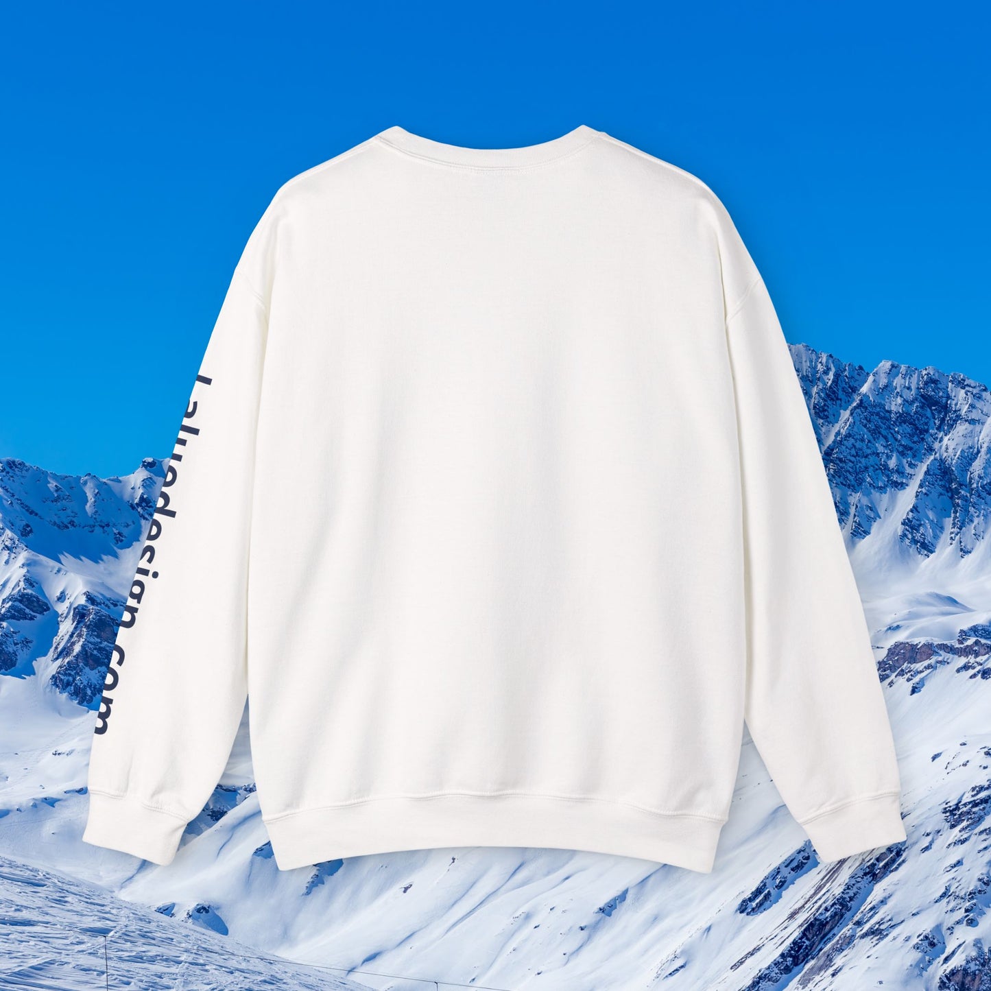 Après Ski Sweatshirt A white crewneck sweatshirt shown from the back, featuring black vertical text printed down one sleeve, set against a bright blue sky and snowy mountain background.