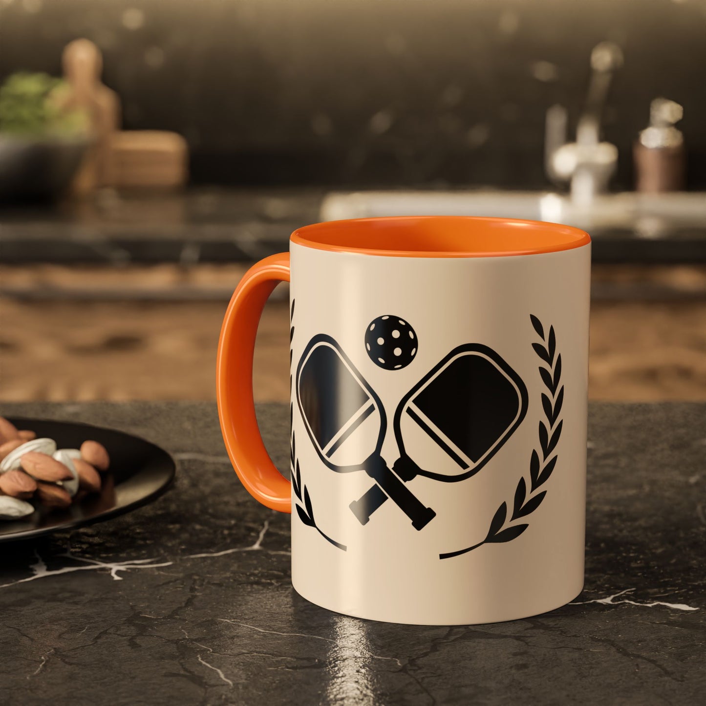 pickleball mug A ceramic mug with an orange handle and interior, featuring a black ping-pong graphic on a cream-colored exterior, set on a dark kitchen countertop.