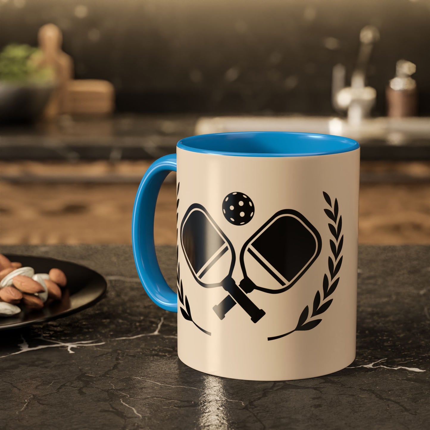 pickleball mug A ceramic mug with a blue interior and handle, featuring a black graphic of ping-pong paddles, a ball, and laurel leaves on a cream background, set on a dark kitchen countertop.