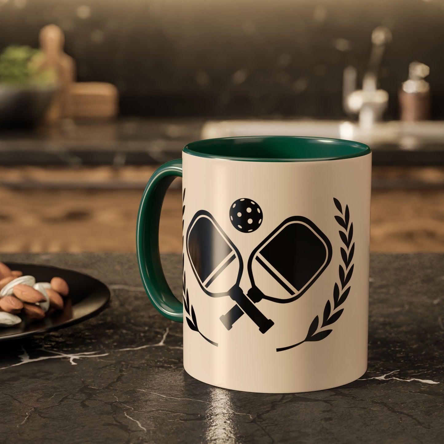 pickleball mug A ceramic mug with a cream-colored exterior and a dark green interior, featuring a black graphic of crossed paddles, a ball, and laurel leaves. The mug is set on a dark marble countertop in a blurred kitchen environment.