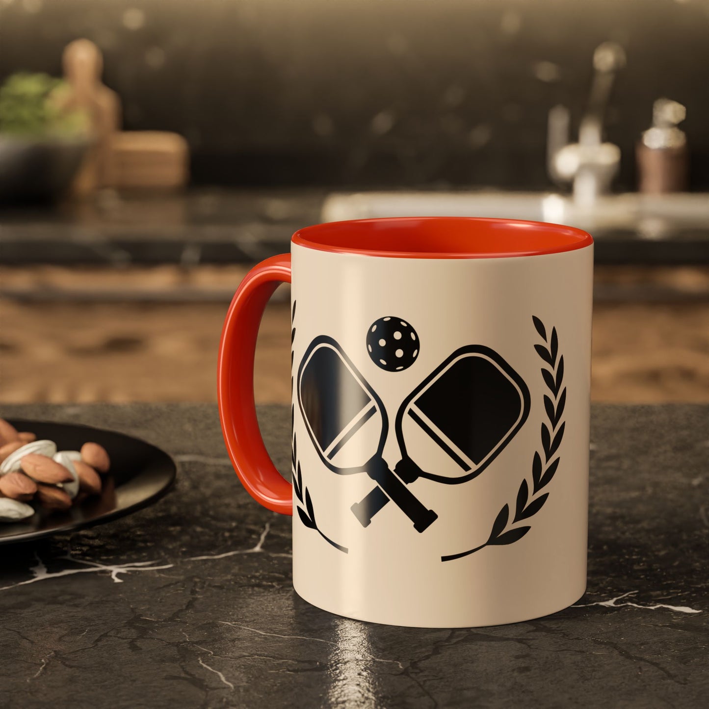 pickleball mug A ceramic mug with a red interior and handle, featuring a black graphic of table tennis paddles, a ball, and laurel leaves on a cream background, set on a dark countertop in a blurred kitchen environment.