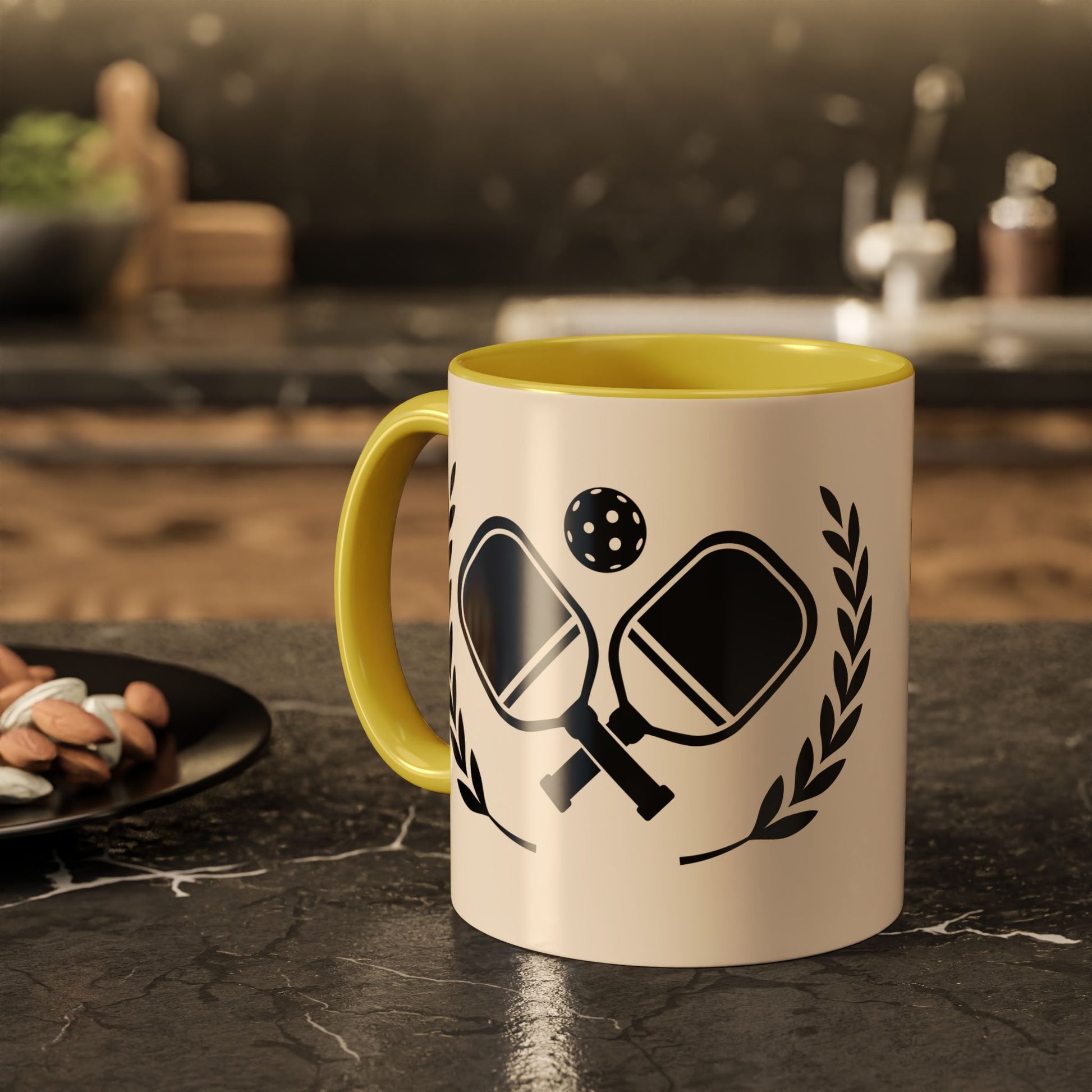 pickleball mug A ceramic mug with a yellow handle and interior, featuring a black graphic of table tennis paddles, a ball, and laurel leaves on a cream-colored exterior, set on a dark kitchen countertop.