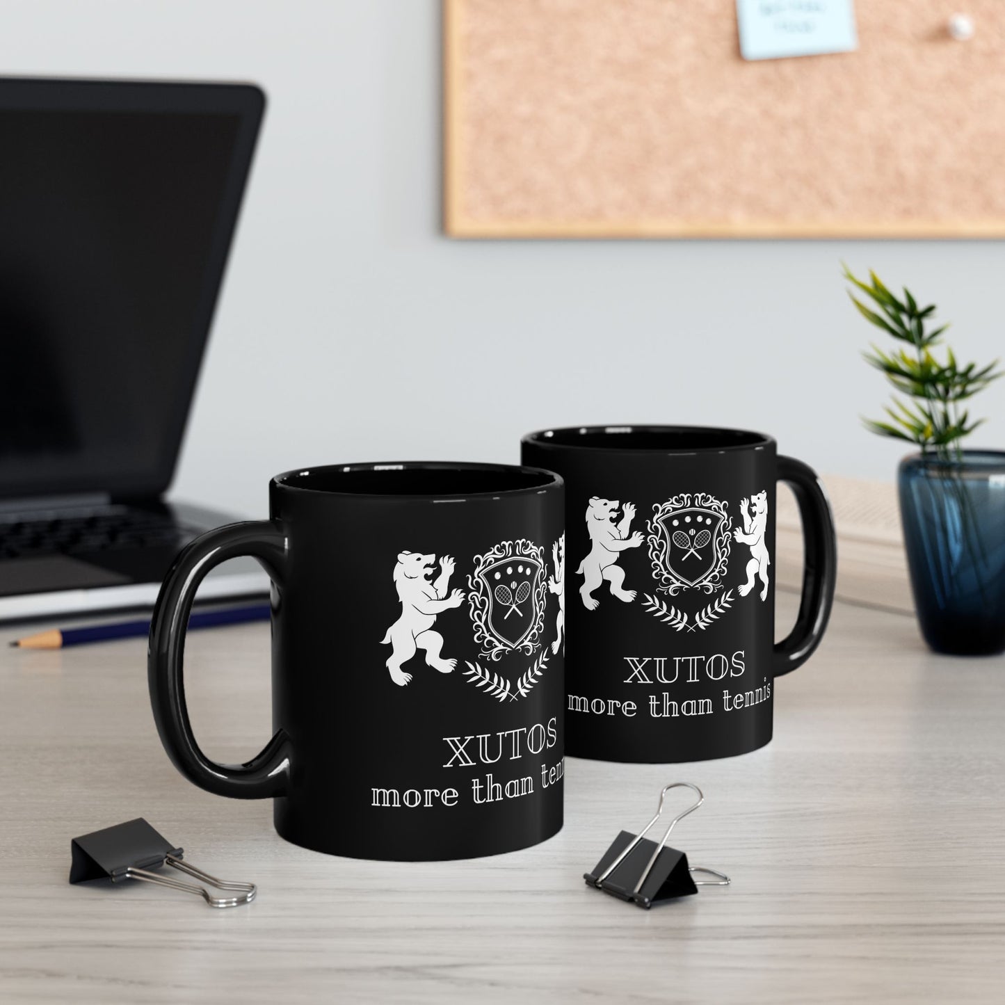 Two Black XUTOS mug with white designs and text on a desk with office supplies.