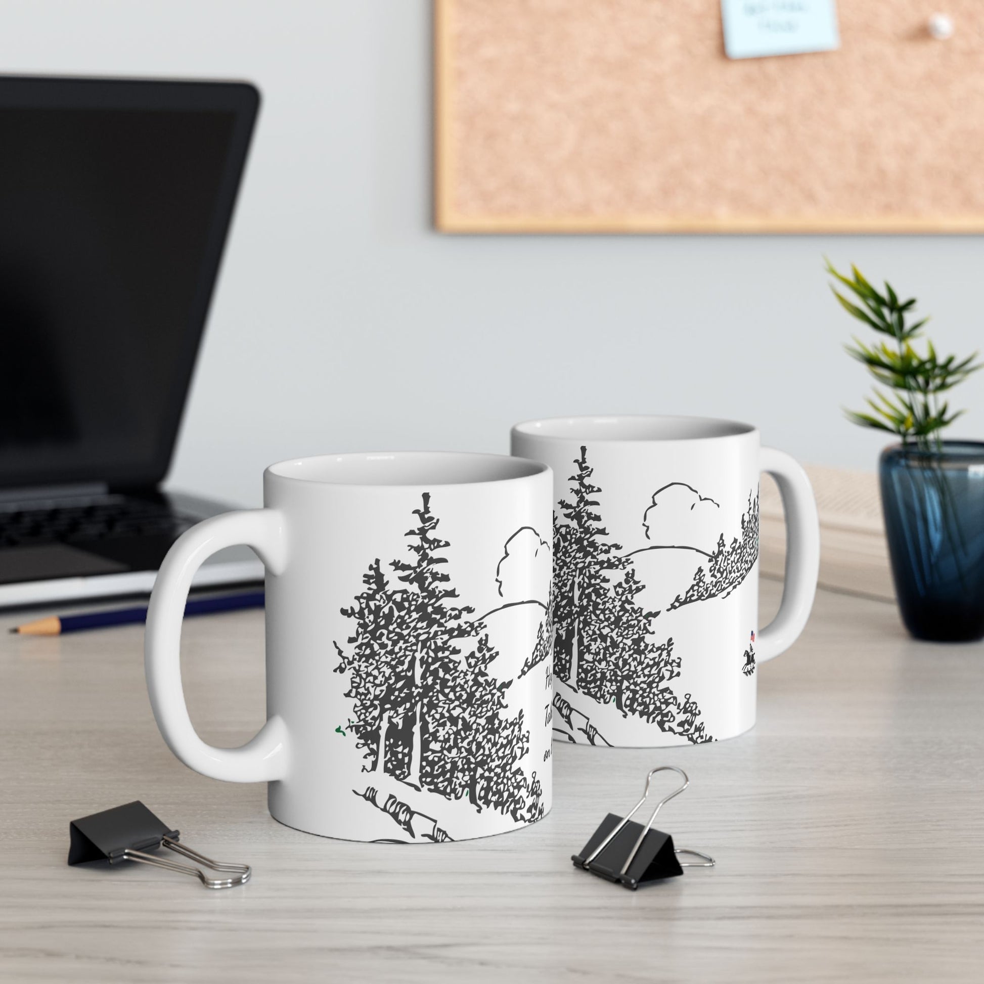 Two mugs with nature-themed designs on a desk with office supplies.