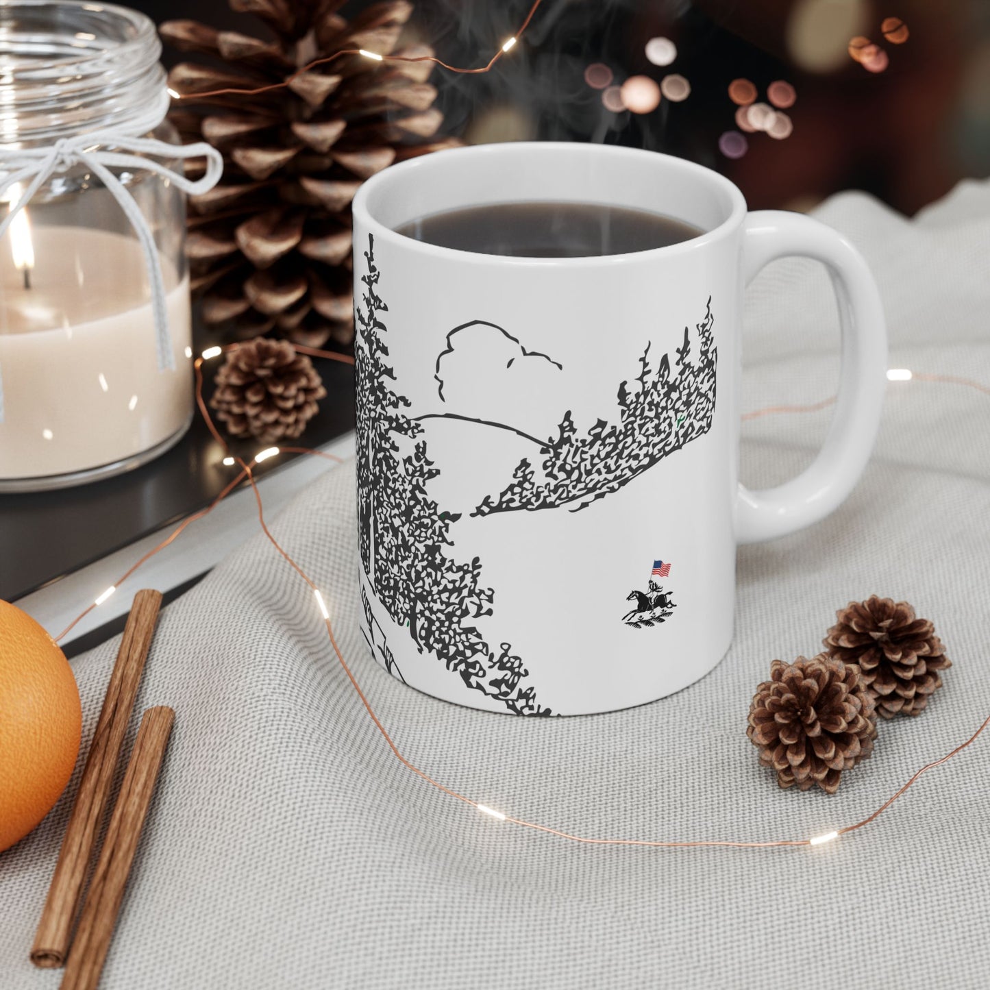 White mug with a black landscape design on a table with decorative items