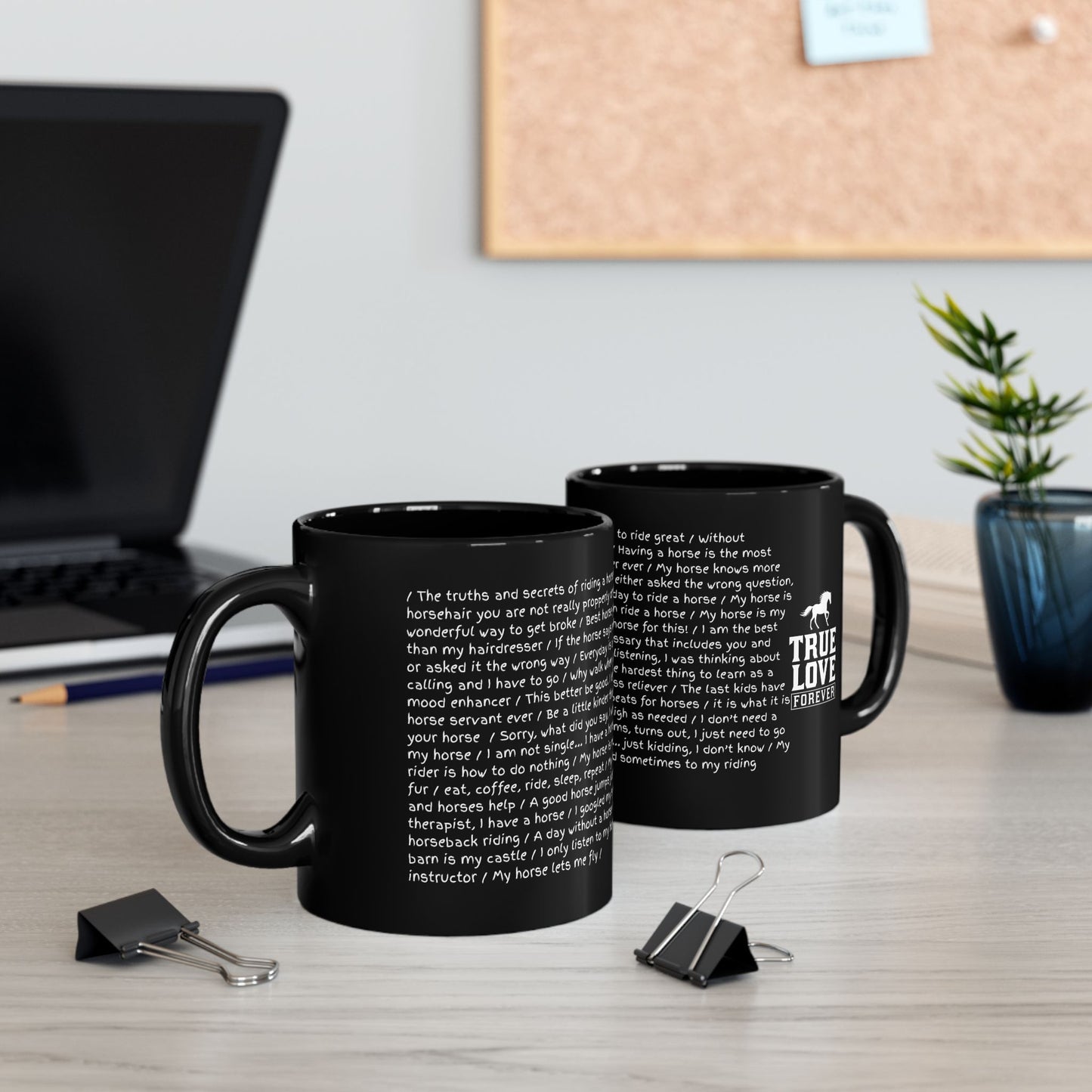Two black mugs with text on a desk with a laptop and plant in the background