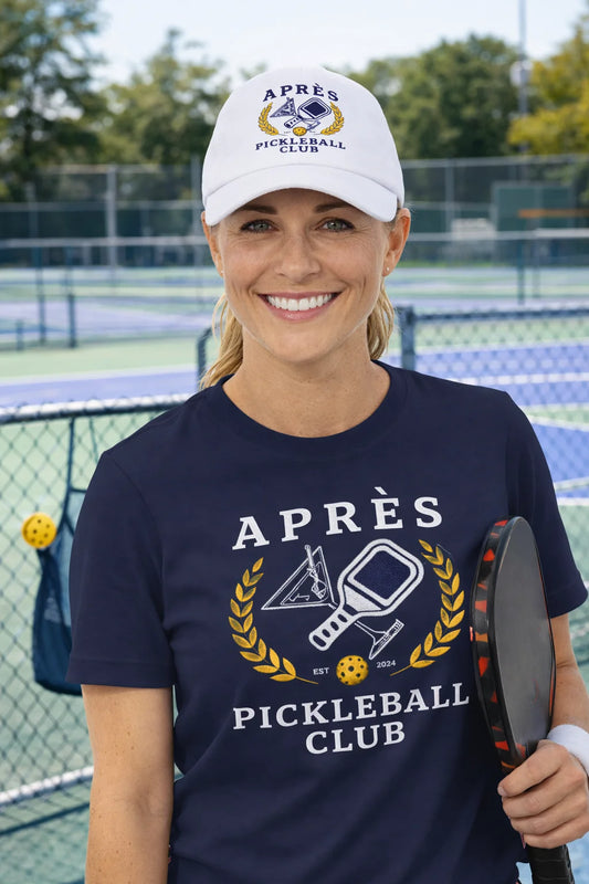 Woman on a pickleball court wearing an 'Après Pickleball Club' shirt and cap.