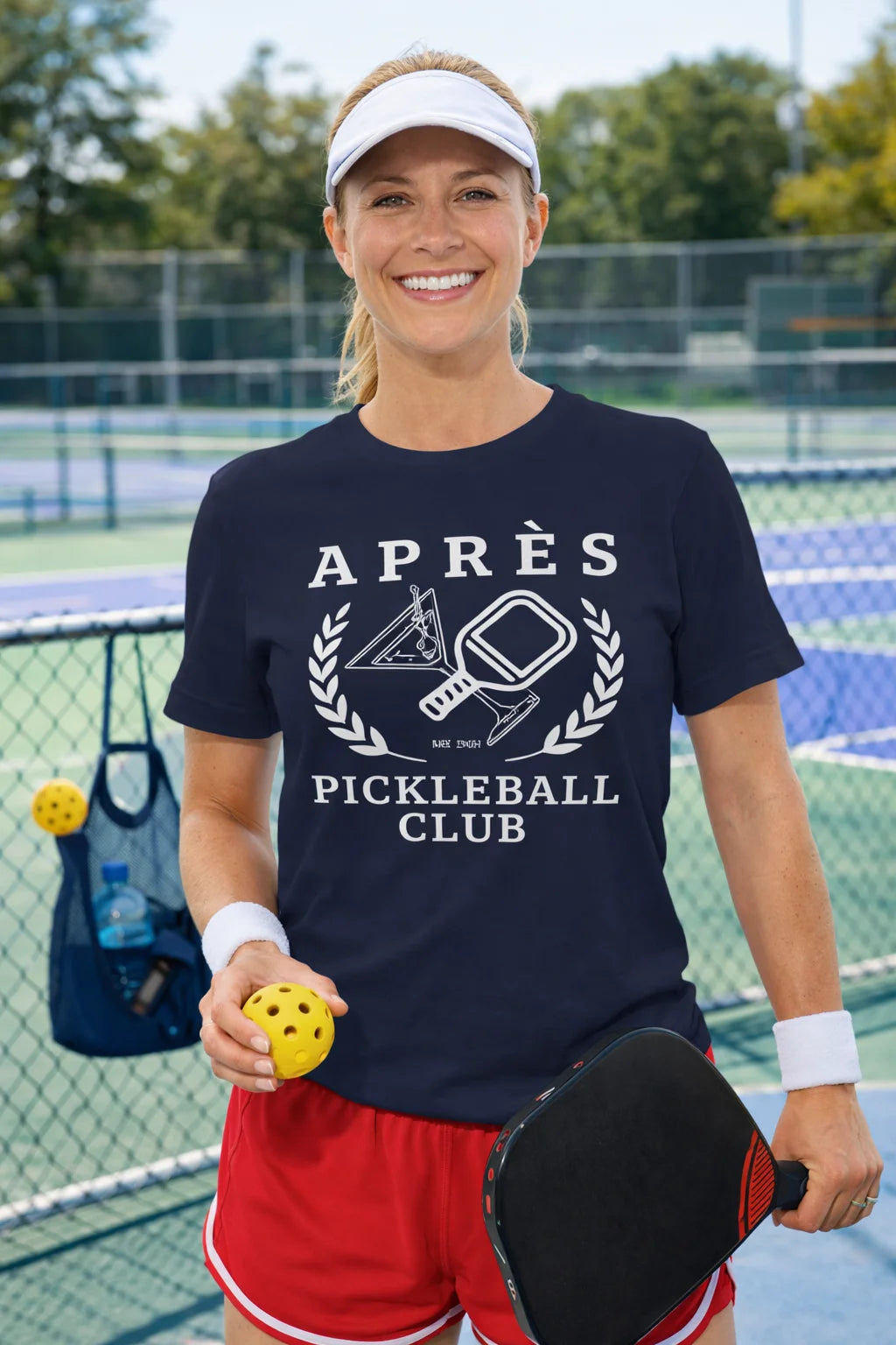 Funny Pickleball Shirt Woman on a pickleball court wearing an 'Après Pickleball Club' shirt, holding a pickleball and paddle.