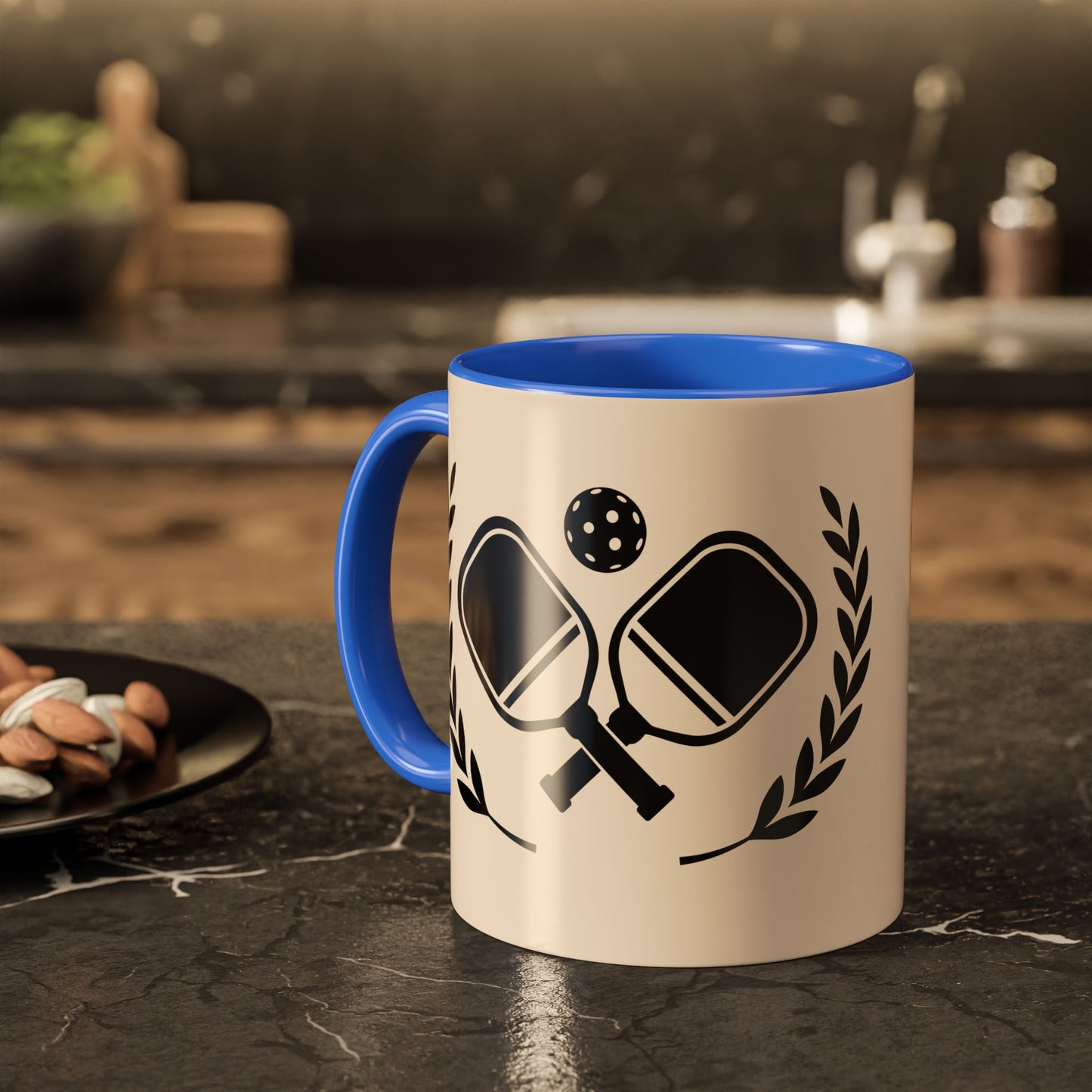 pickleball mug A ceramic mug with a blue interior and handle, featuring a black graphic of ping-pong paddles, a ball, and laurel leaves on a cream-colored exterior, set on a dark kitchen countertop.