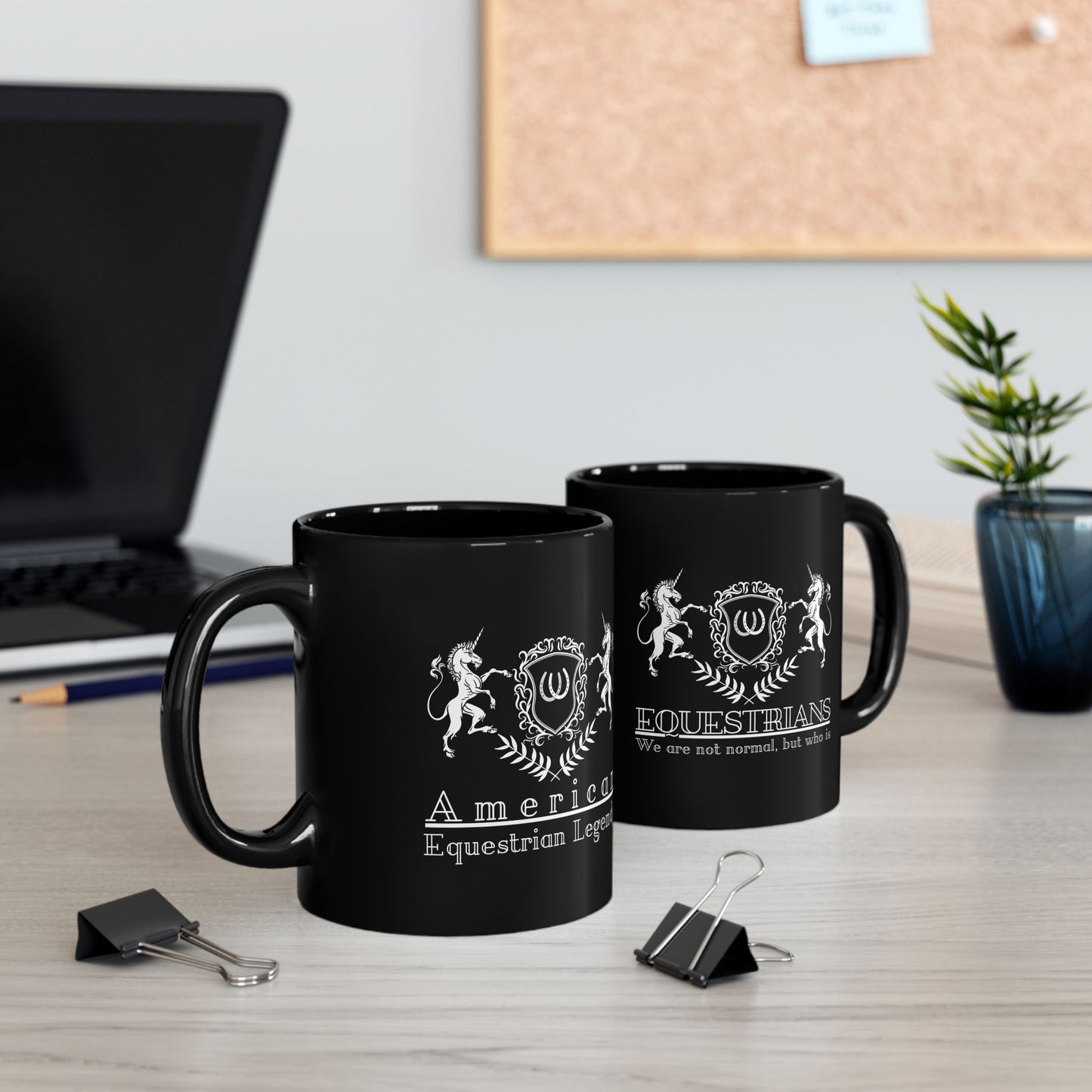 Two black mugs with white designs on a desk with office supplies and a plant.