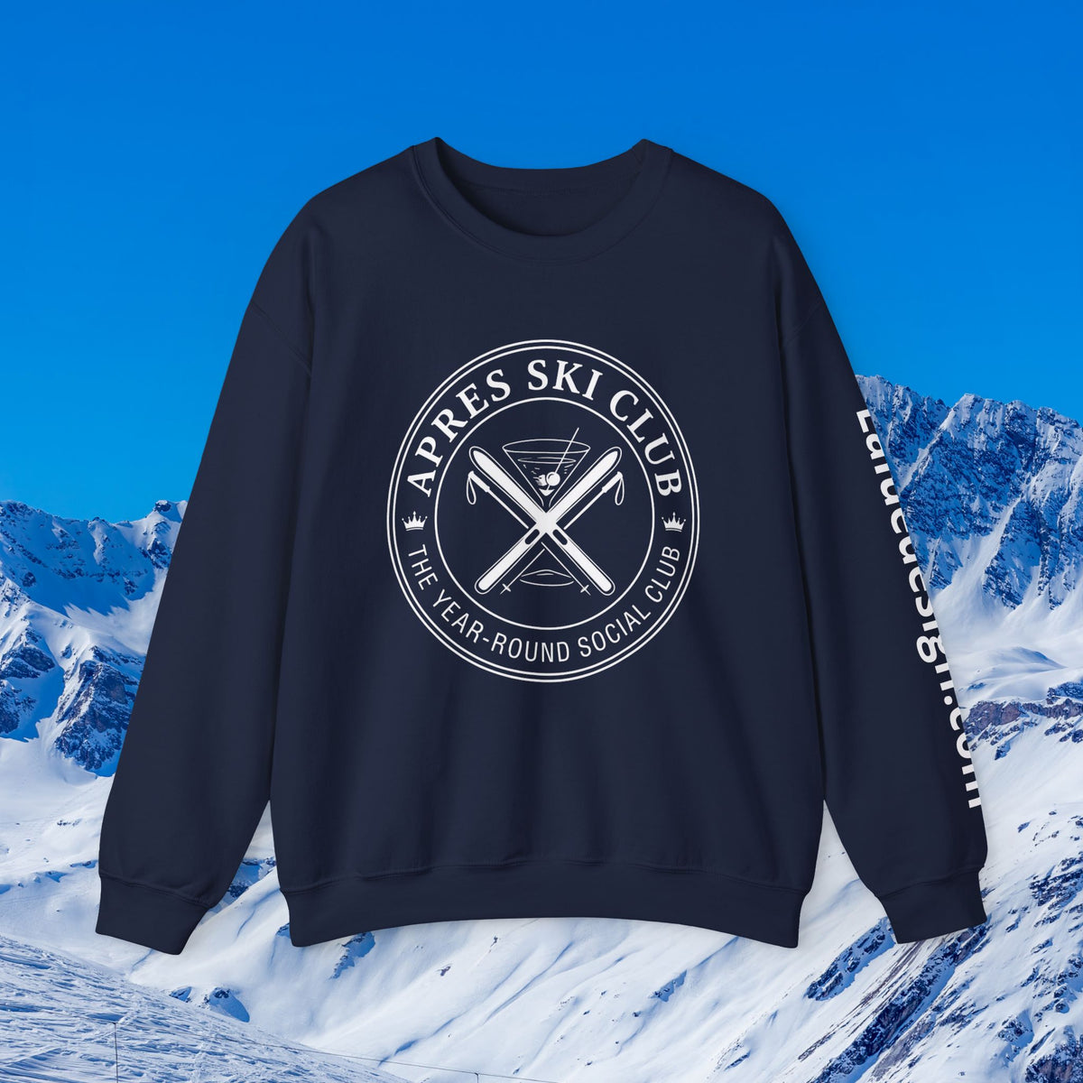 Apres Ski sweater A black crewneck sweatshirt with a white circular graphic reading 'APRES SKI CLUB' and crossed skis on the chest, plus white text down the sleeve, shown against a snowy mountain and blue sky background.
