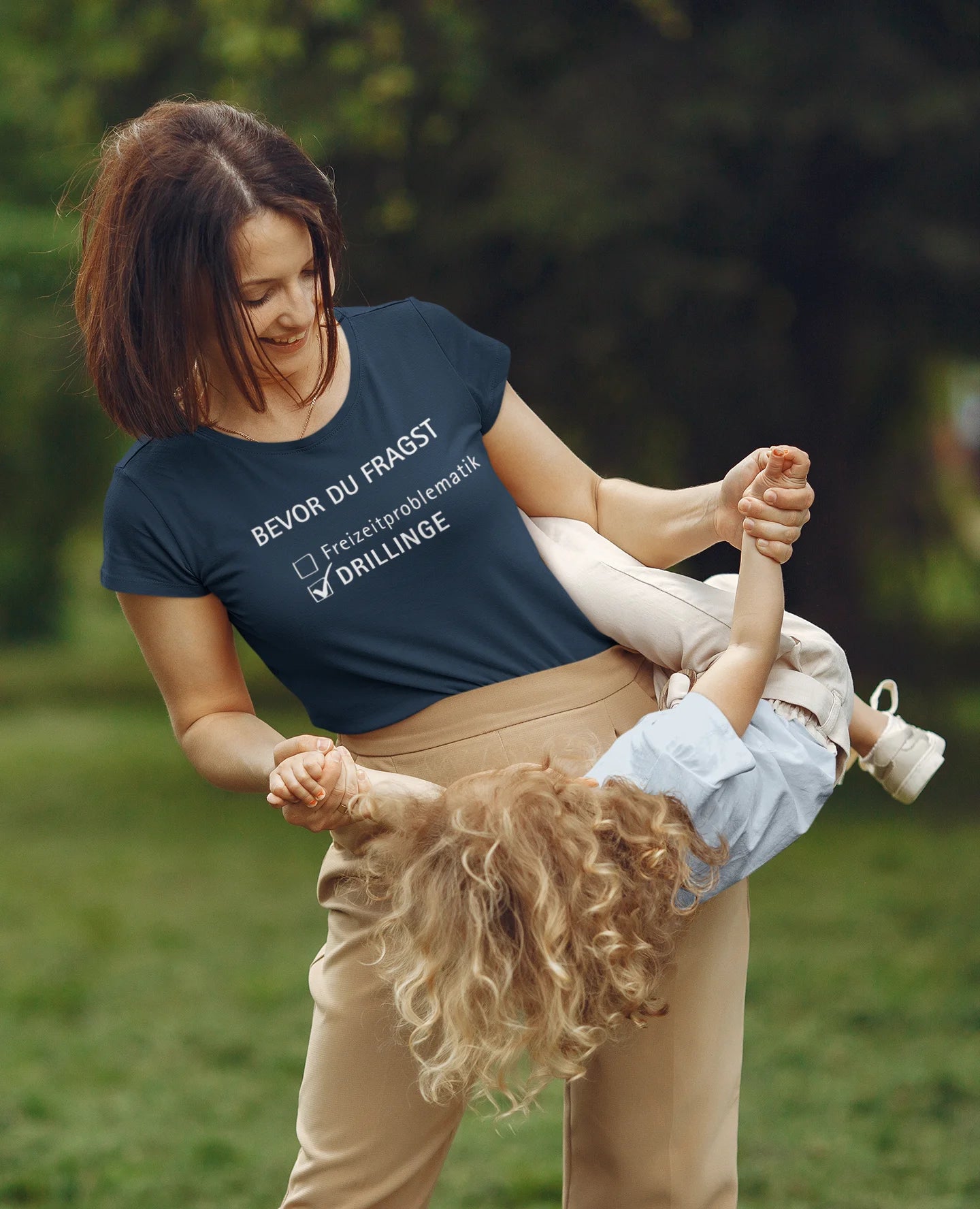 Gift for Triplets Woman playing with a child in a park wearing a t-shirt with text.