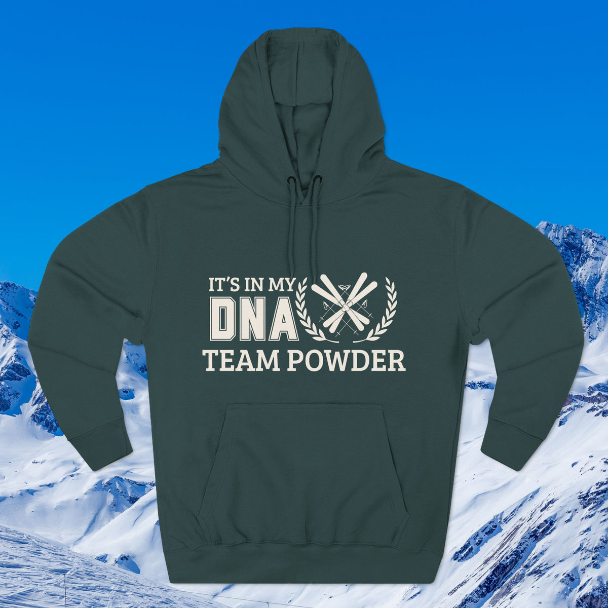 Its in my DNA A dark green pullover hoodie with a white graphic print reading 'IT'S IN MY DNA TEAM POWDER' and crossed ski poles, shown against a snowy mountain and blue sky background.