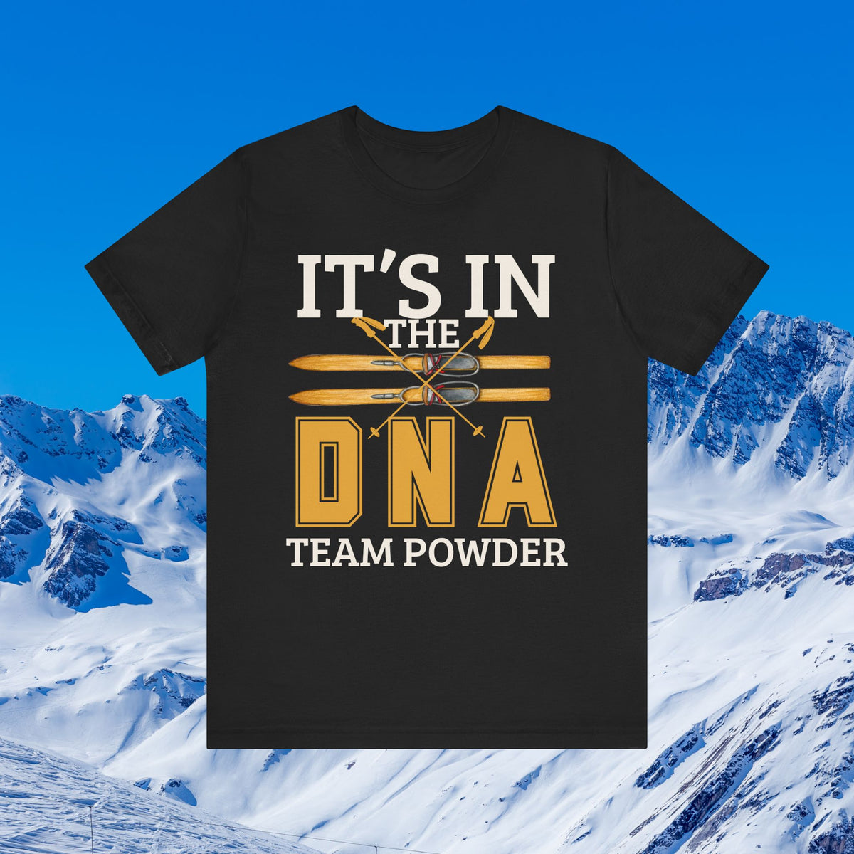 Its in the DNA A black short-sleeve graphic T-shirt displayed against a snowy mountain and blue sky background. The shirt features a large front print reading “IT’S IN THE DNA TEAM POWDER” with crossed skis and a ski boot graphic in white and gold.