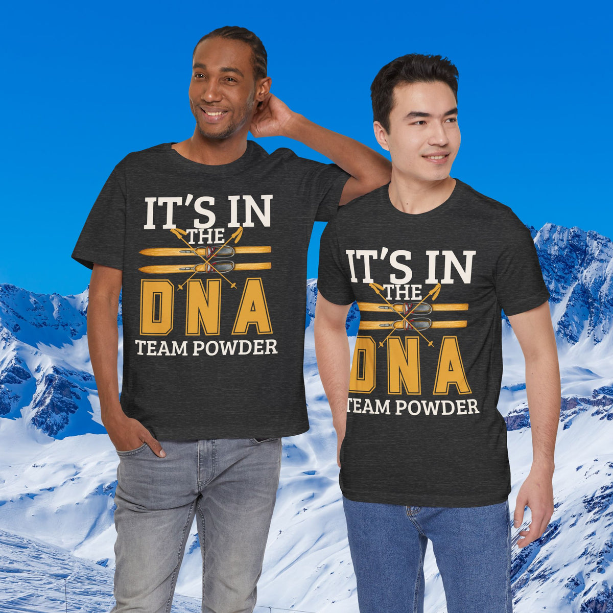 Its in the DNA Two men modeling matching dark gray graphic t-shirts with the text 'IT'S IN THE DNA TEAM POWDER' in white and yellow, set against a snowy mountain background.