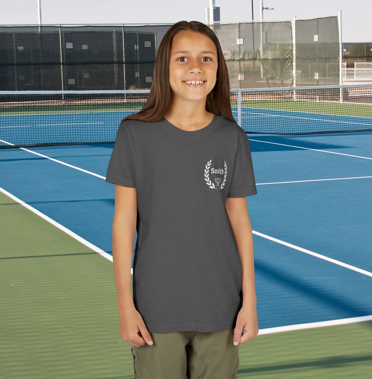 Junior tennis shirts Young girl standing on a tennis court wearing a gray t-shirt with a logo.