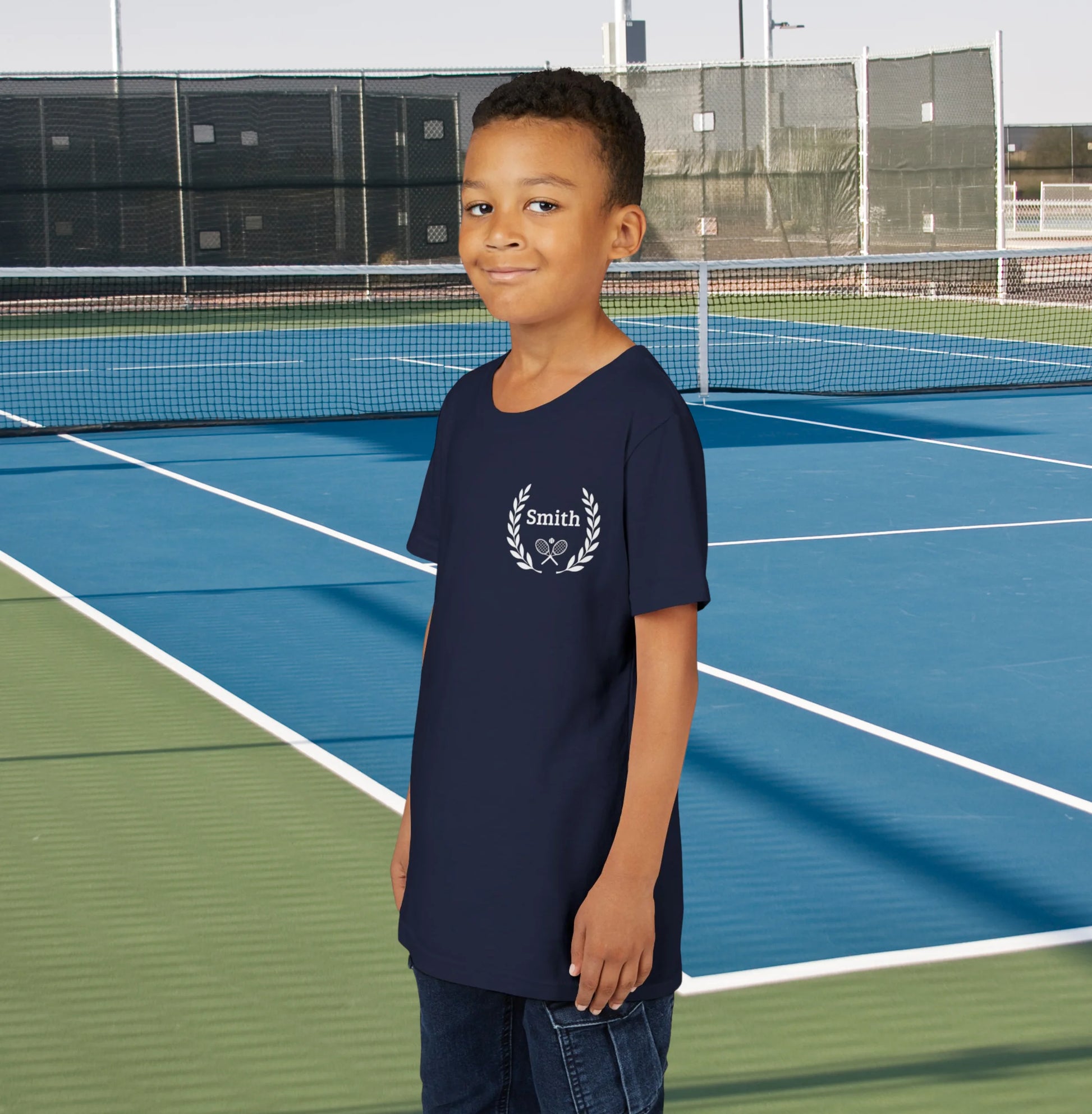 Junior tennis shirts Child wearing a navy blue t-shirt with 'Smith' logo on a tennis court