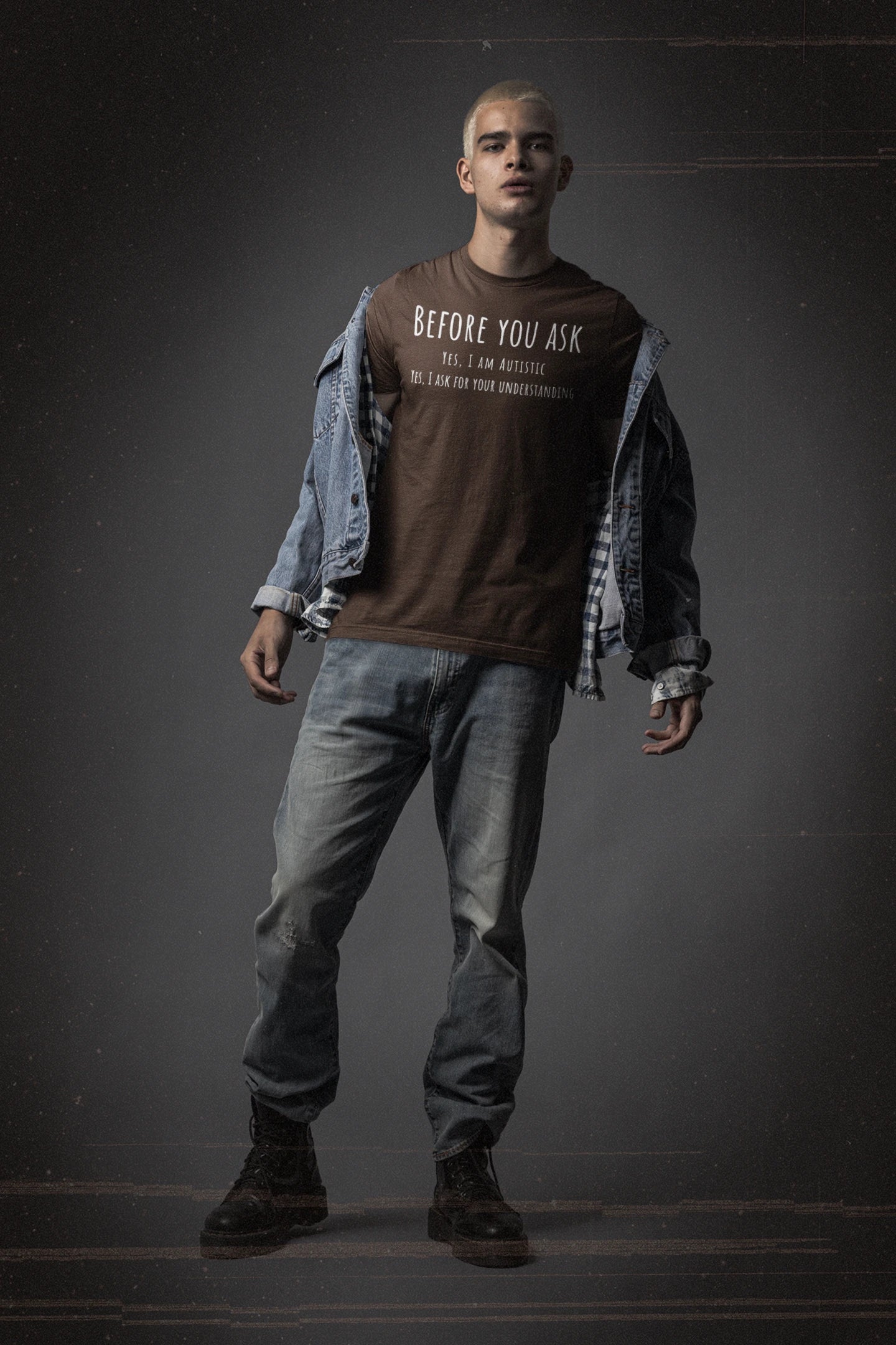 Person wearing a brown shirt with text, denim jacket, and jeans on a dark background