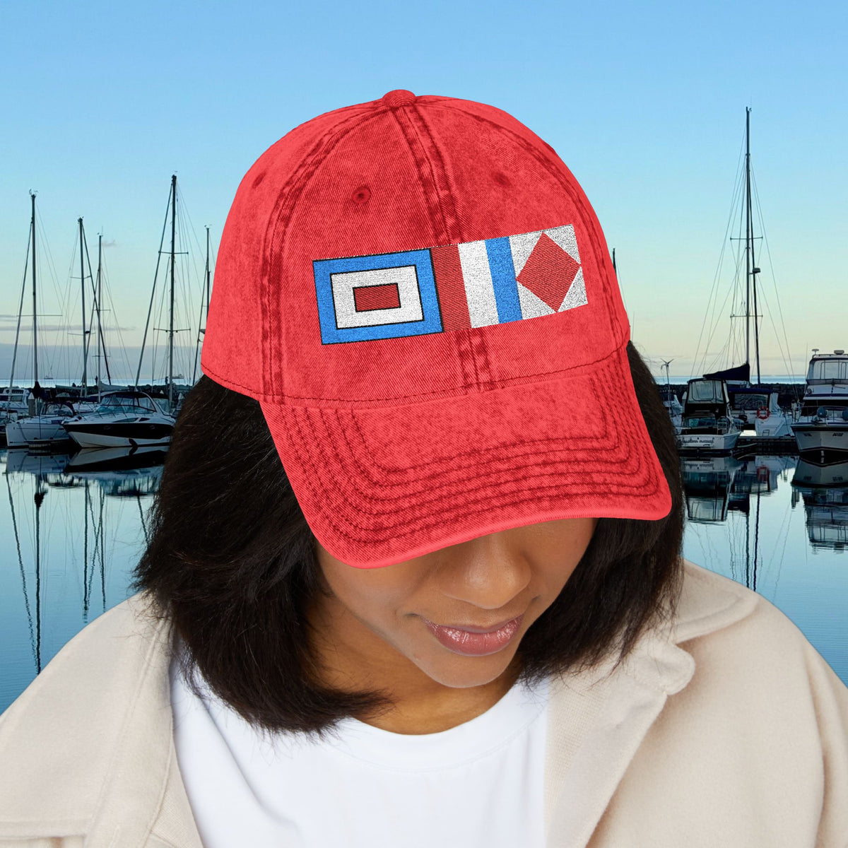 Nautical caps A person wearing a red baseball cap with two nautical flag patches, photographed outdoors in front of a marina at dusk.