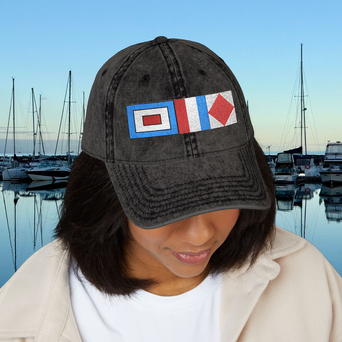 Nautical caps A person wearing a dark gray washed baseball cap with a nautical flag patch, set against a background of a marina at dusk.