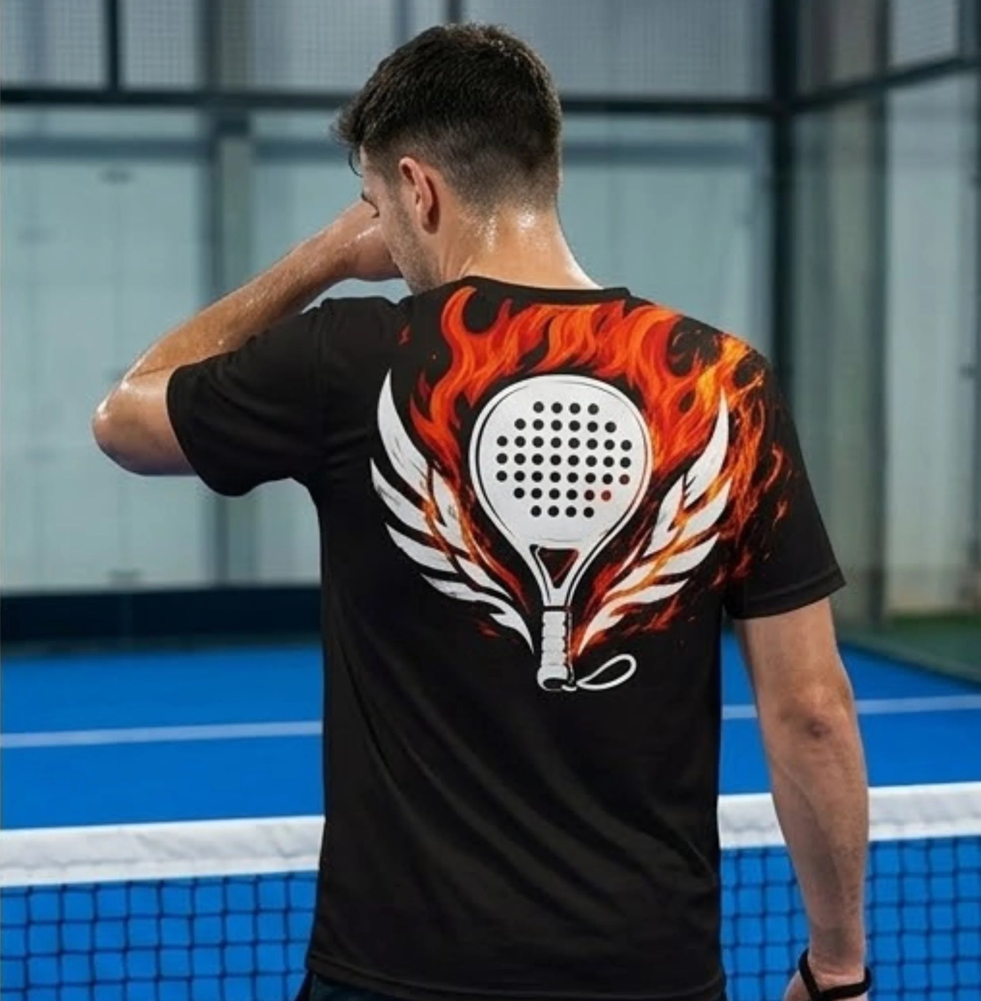 Performance Padel Shirt Person wearing a black t-shirt with a fiery paddle design on a sports court