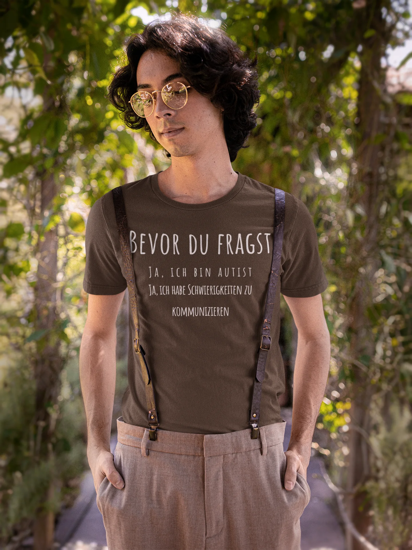 Man wearing a brown t-shirt with text standing outdoors among trees