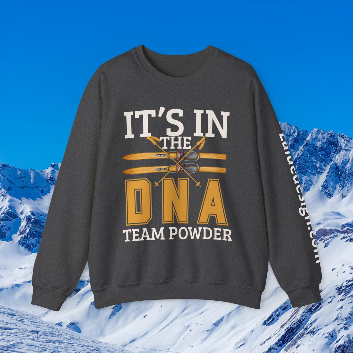 Ski Sweatshirt A dark gray crewneck sweatshirt with a graphic print reading 'IT'S IN THE DNA TEAM POWDER' in white and gold, displayed against a snowy mountain background under a blue sky.