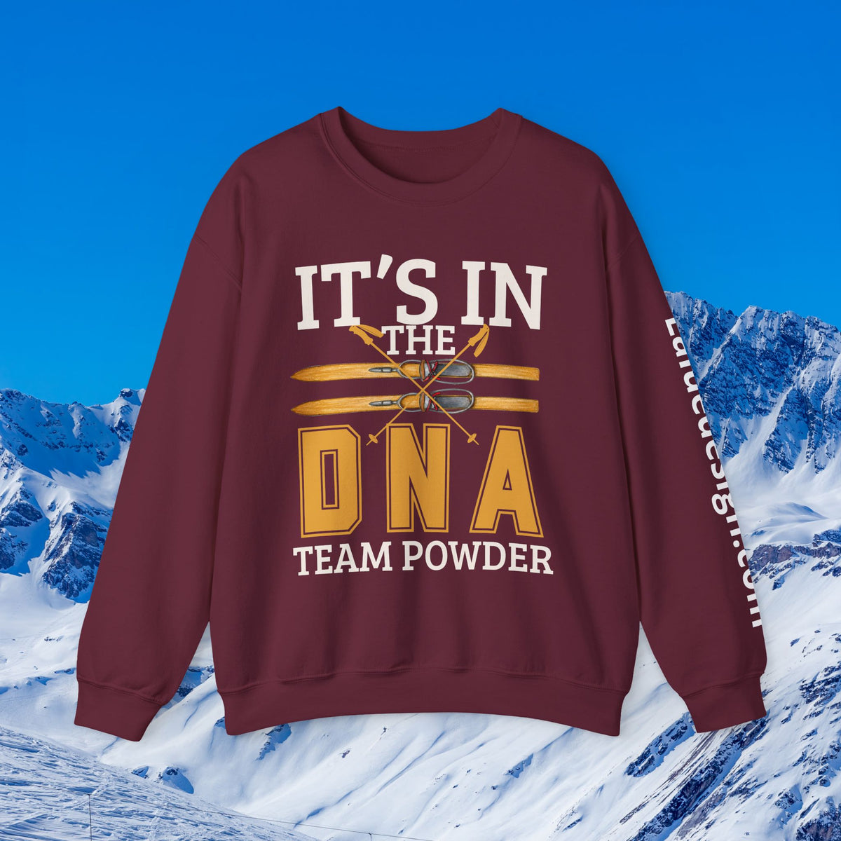Ski Sweatshirt A maroon crewneck sweatshirt with a ski-themed graphic reading 'IT'S IN THE DNA TEAM POWDER' in white and yellow, displayed against a snowy mountain and blue sky background.