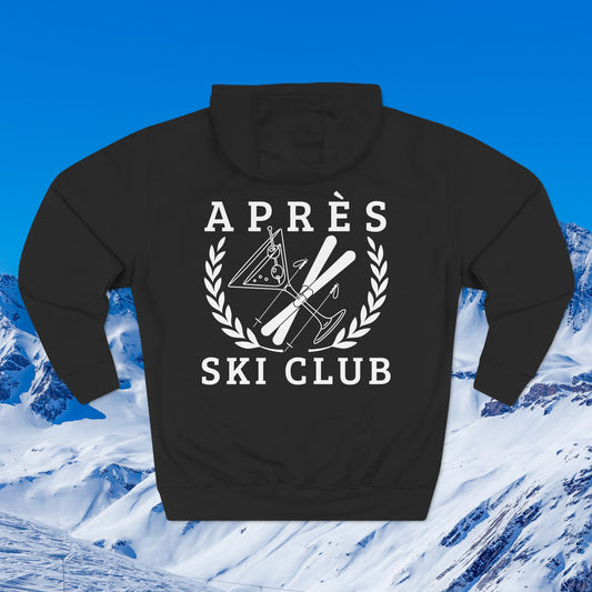 Ski hoodie A black pullover hoodie shown from the back, featuring a white graphic print that reads 'APRÈS SKI CLUB' with crossed skis, ski poles, and a snowboard enclosed by a laurel wreath. The hoodie is centered against a scenic background of snowy mountains under a bright blue sky.
