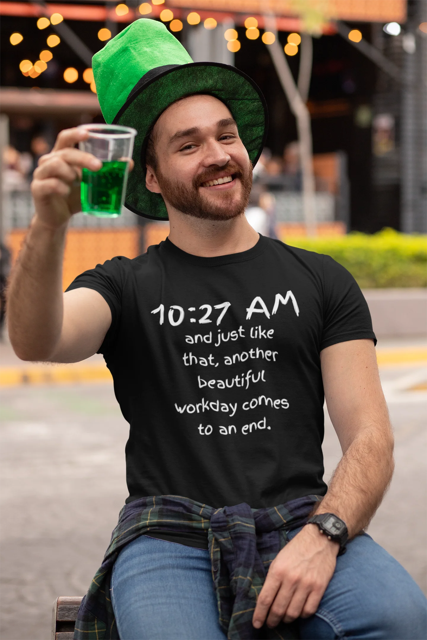 funny office shirt Man wearing a black t-shirt with text, holding a green drink, and wearing a green hat in an outdoor setting.