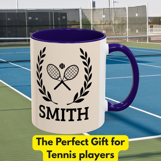 Tennis Coffee Mug A white ceramic mug with a dark purple interior and handle, featuring a black graphic of crossed tennis rackets, laurel leaves, and the name 'SMITH'. The mug is set against a blurred background of a blue and green tennis court, with a yellow banner at the bottom reading 'The Perfect Gift for Tennis players'.