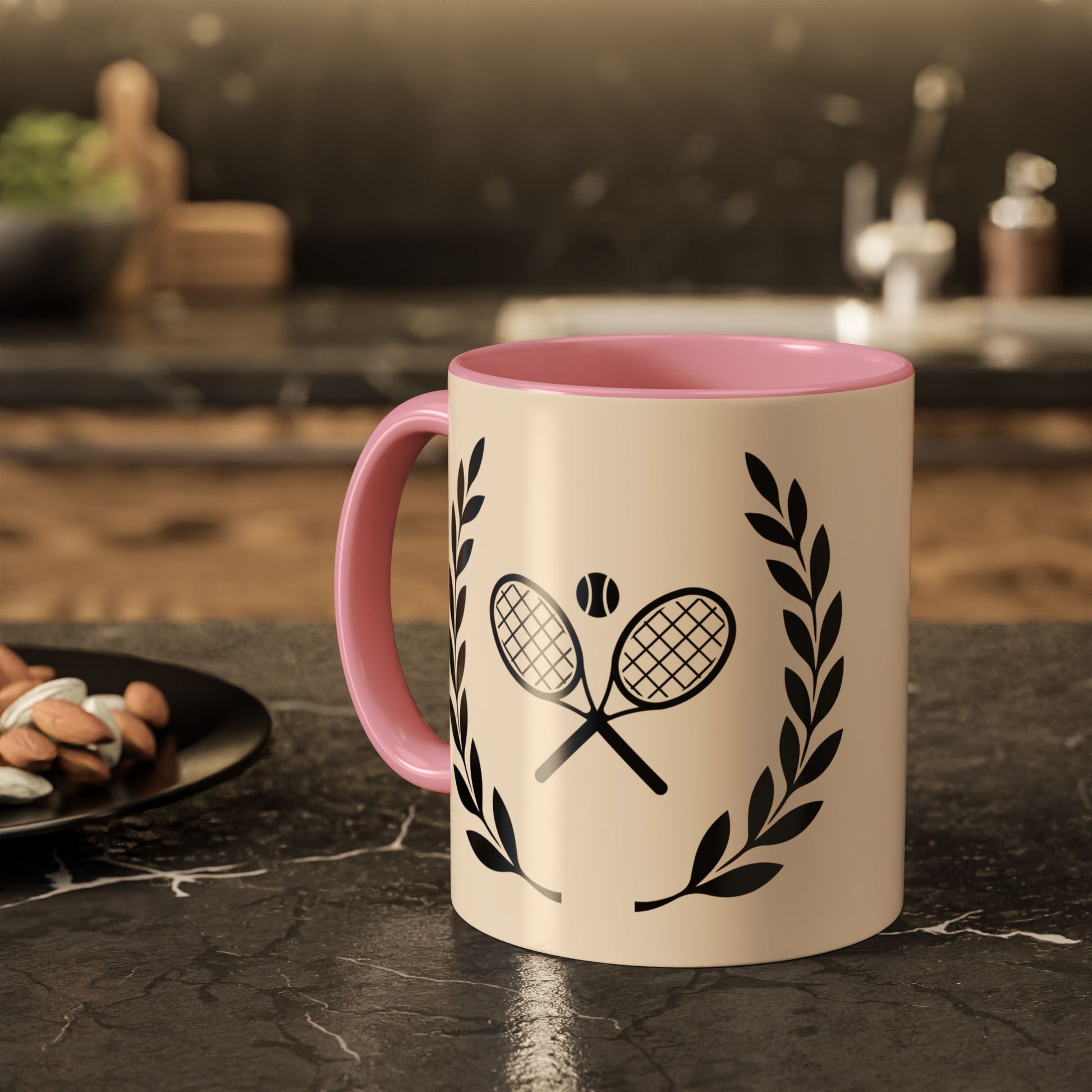Tennis Coffee Mug A ceramic mug with a pink handle and interior, featuring a black graphic of crossed tennis rackets and laurel leaves on a cream-colored exterior, set on a dark kitchen countertop.