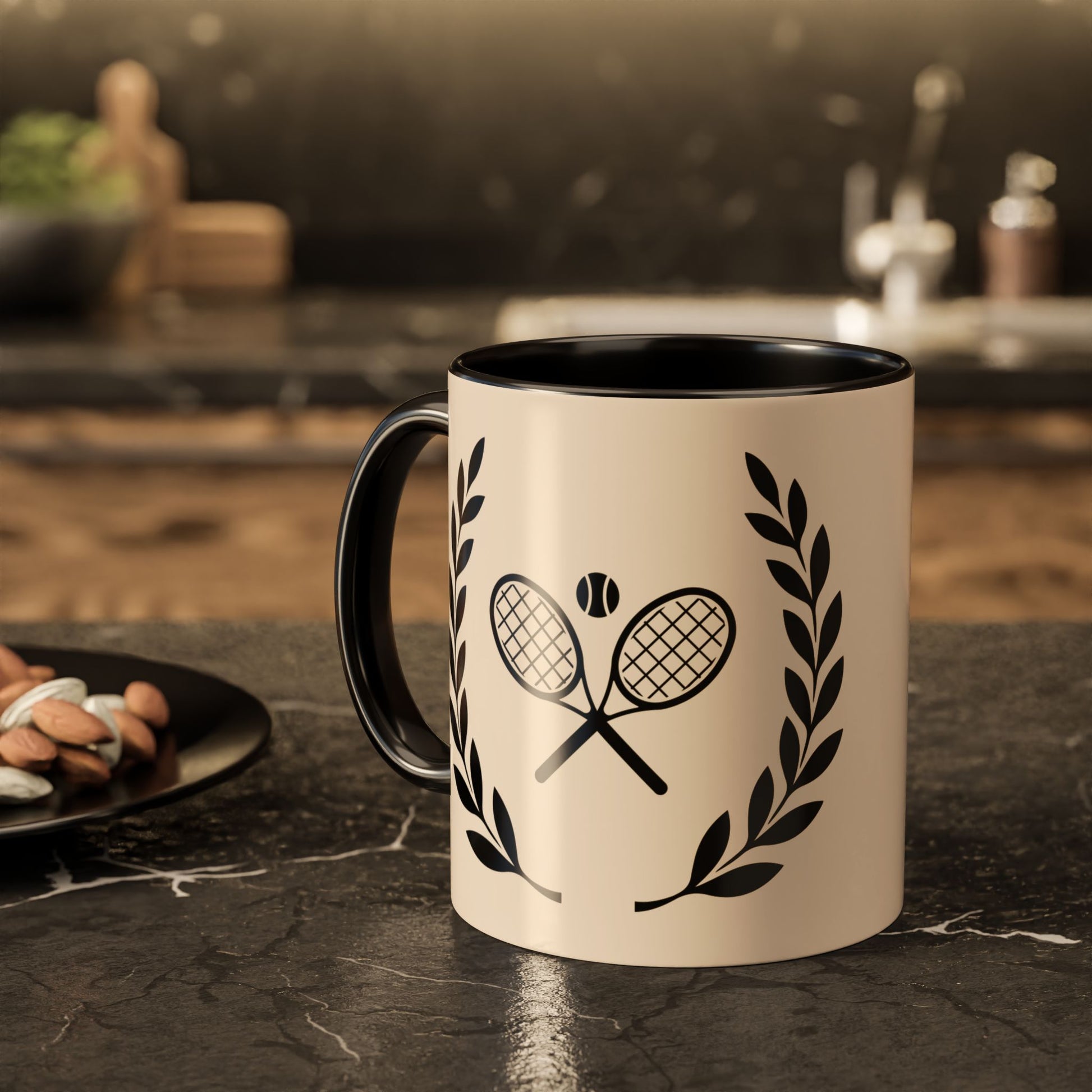 Tennis Coffee Mug A ceramic mug with a cream-colored exterior and black interior/handle, featuring a black graphic of crossed tennis rackets with a tennis ball and laurel wreaths, set on a dark kitchen countertop.