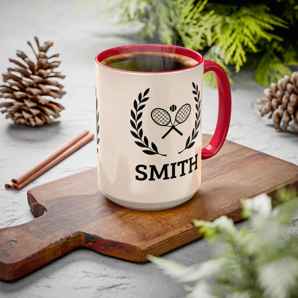 Tennis Coffee Mug A ceramic coffee mug with a red handle and rim sits on a wooden cutting board. The mug is cream-colored with a black graphic of two crossed tennis rackets inside a laurel wreath and the name 'SMITH' printed below.