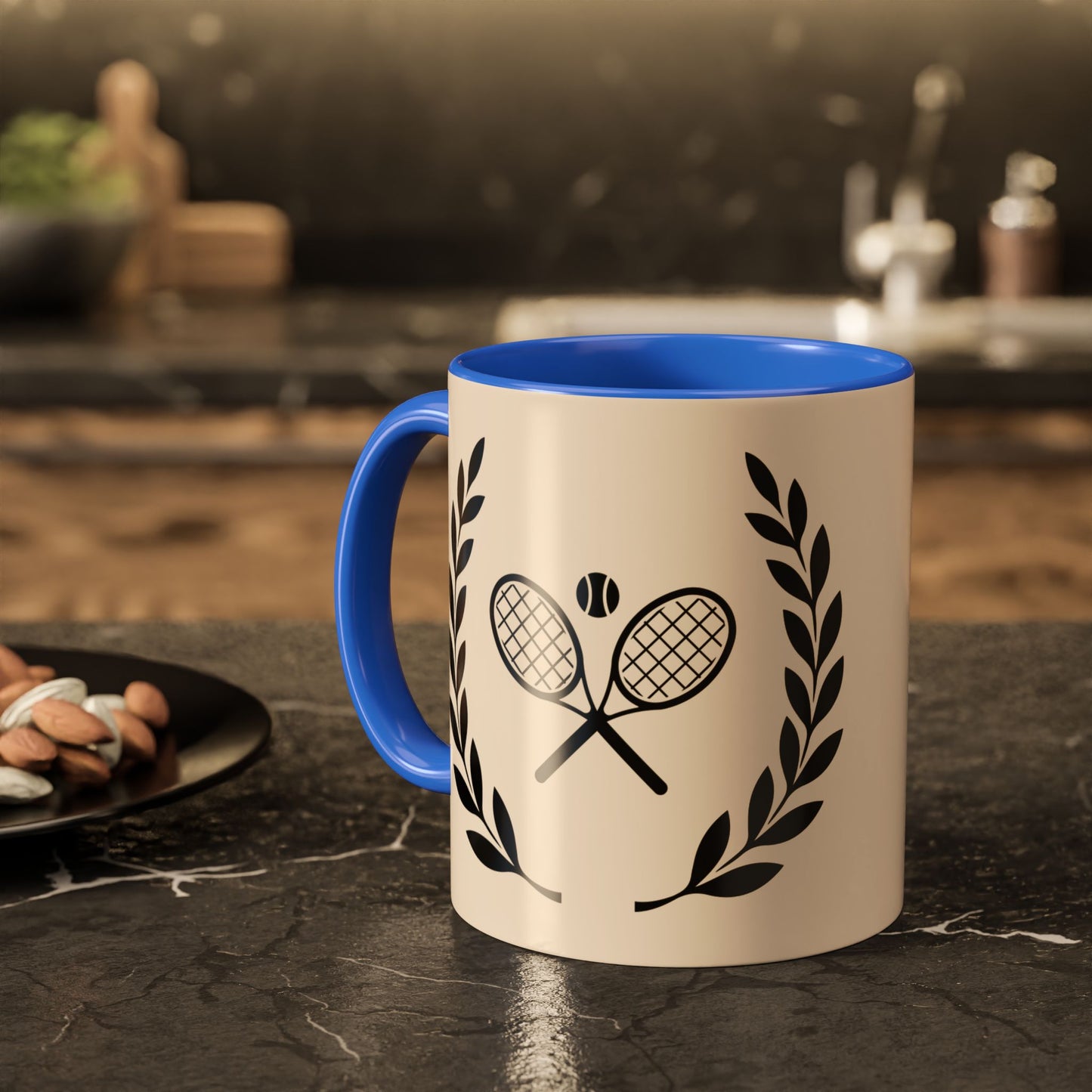 Tennis Coffee Mug A ceramic mug with a cream-colored exterior and a bright blue handle and interior, featuring a black graphic of crossed tennis rackets and laurel leaves. The mug is set on a dark, polished stone countertop with a blurred kitchen background.
