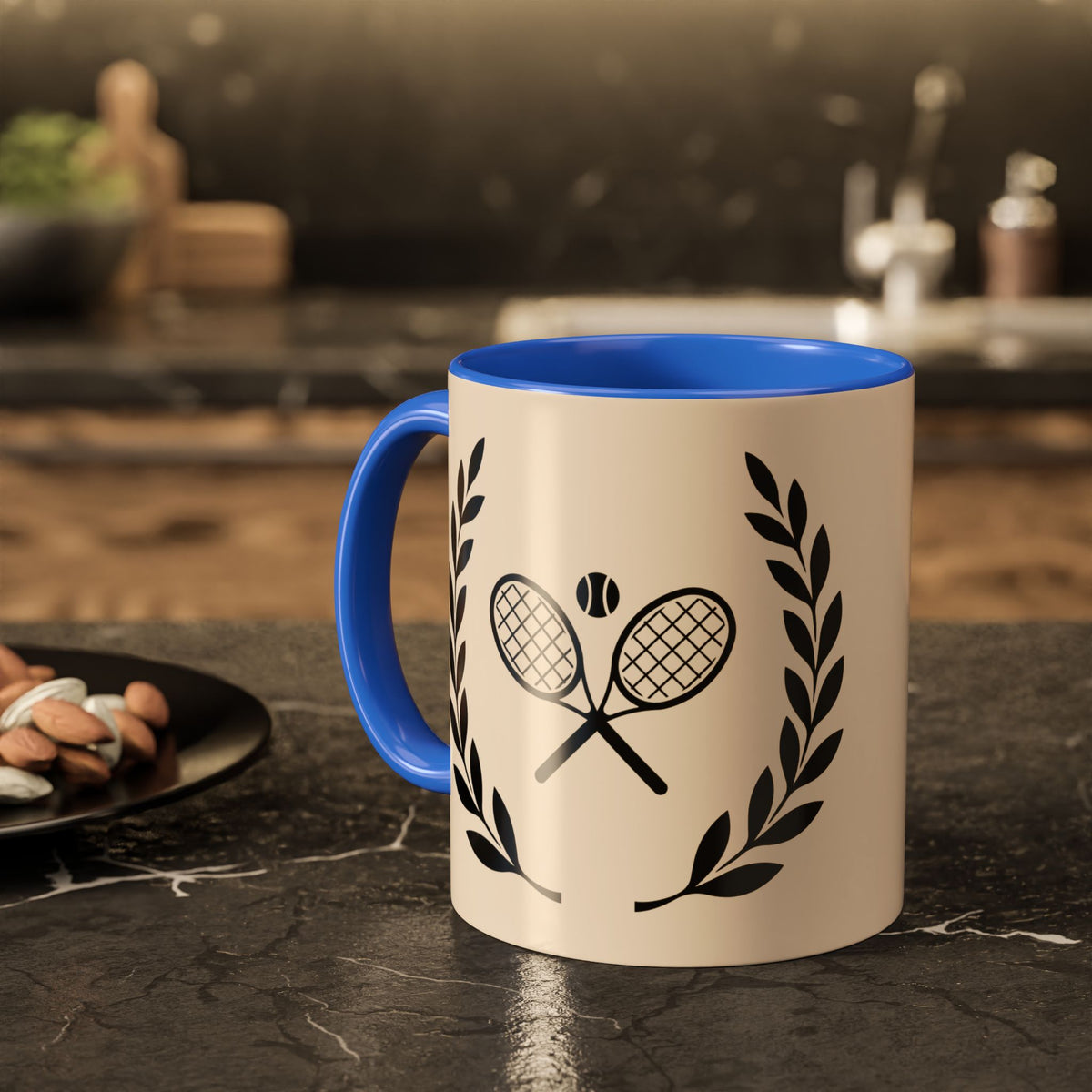 Tennis Coffee Mug A ceramic mug with a cream-colored exterior and a bright blue handle and interior, featuring a black graphic of crossed tennis rackets and laurel leaves. The mug is set on a dark, polished stone countertop with a blurred kitchen background.